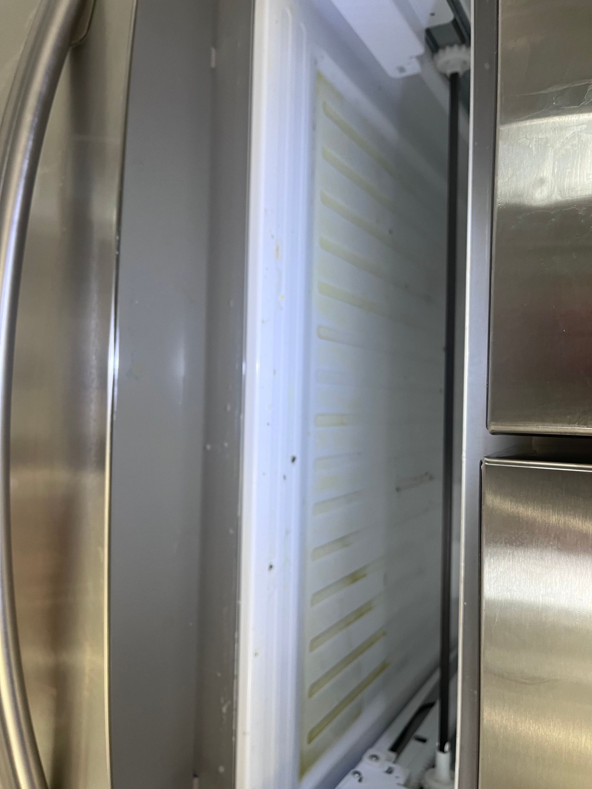 Open refrigerator freezer compartment with white interior, a black vertical bar, and stainless steel door.