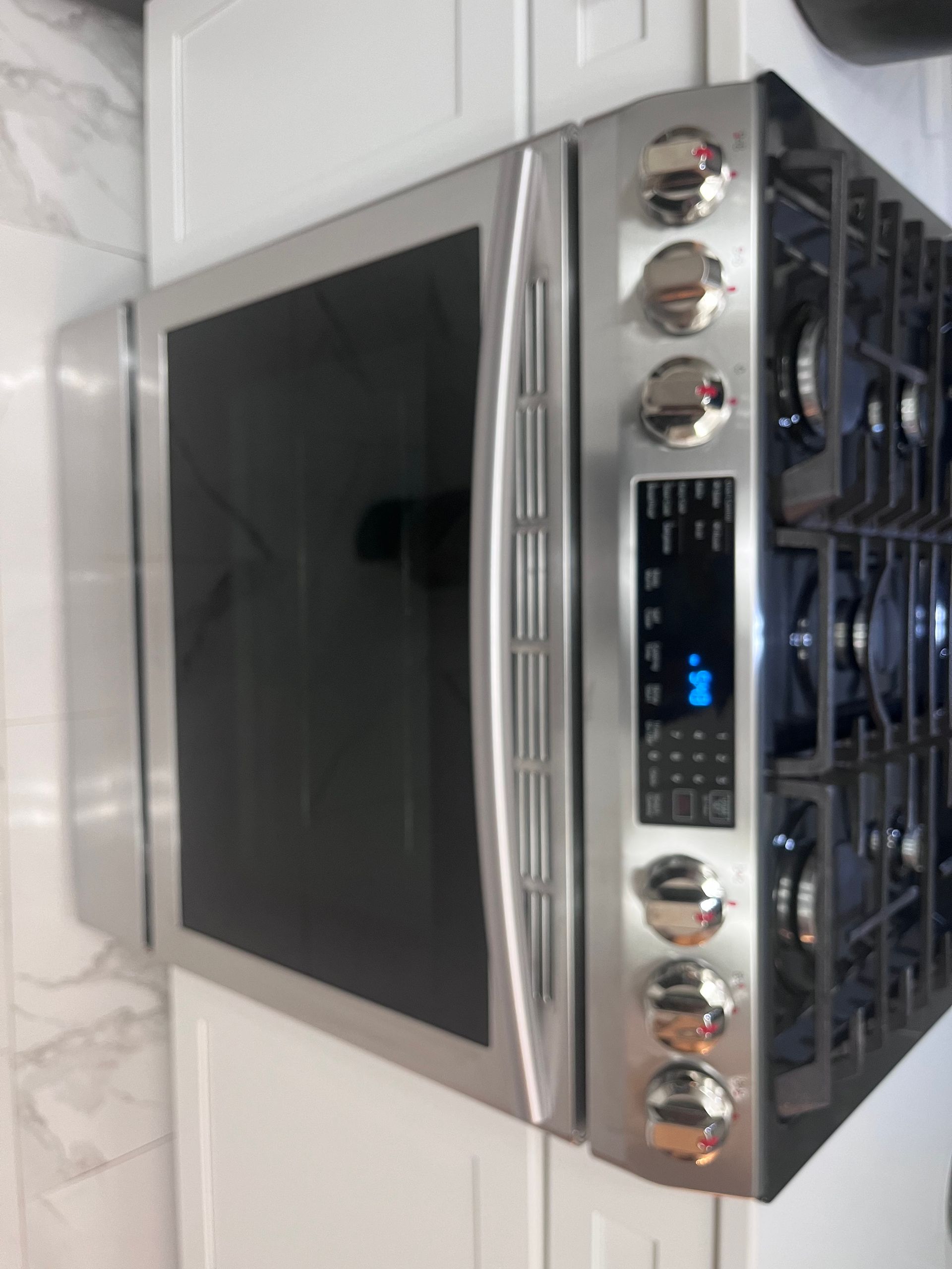 A stainless steel oven and gas stovetop combo built into white cabinets. The oven has a black glass door and digital display.