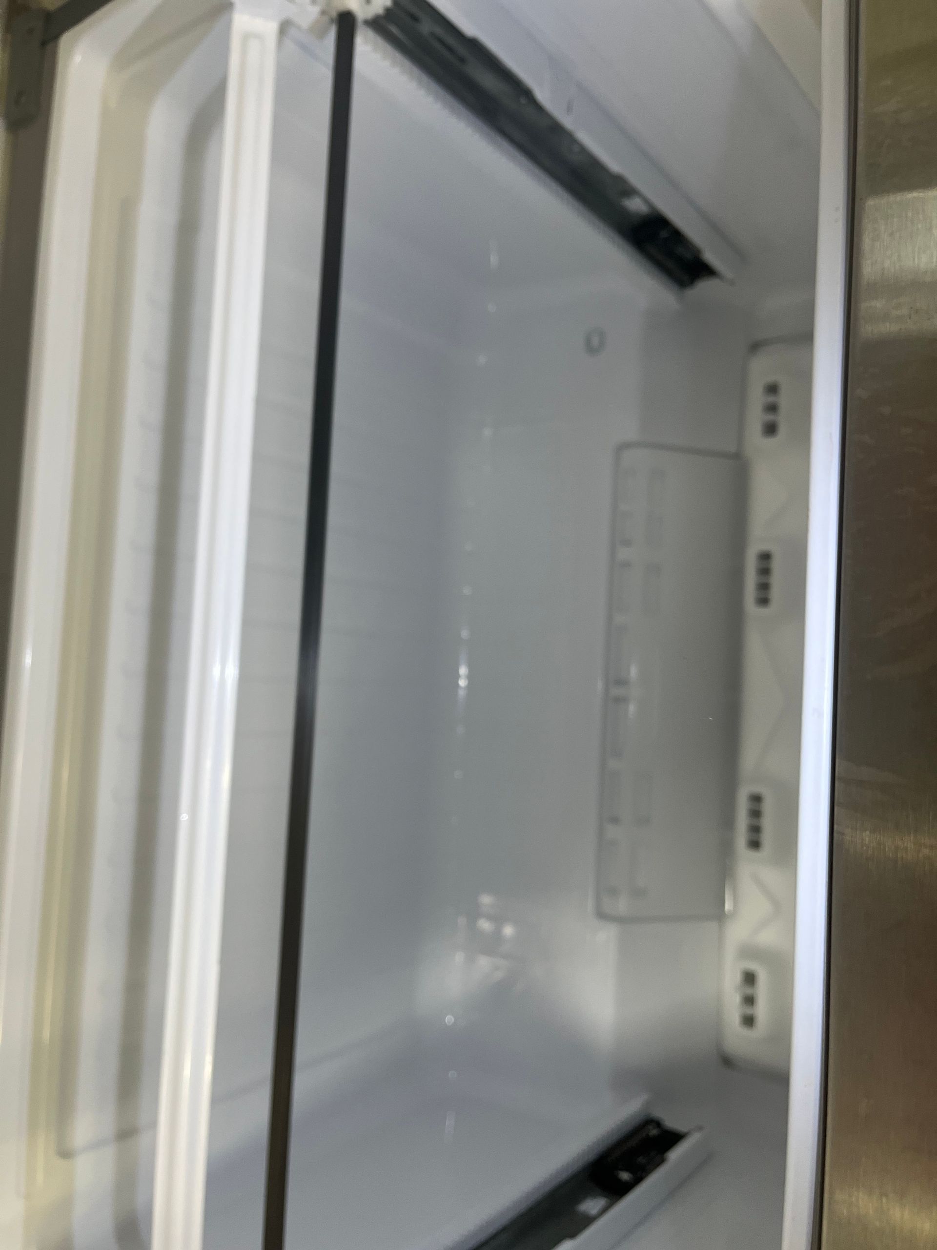 Empty, white refrigerator interior. The inside walls are white and the rails for drawers are visible.