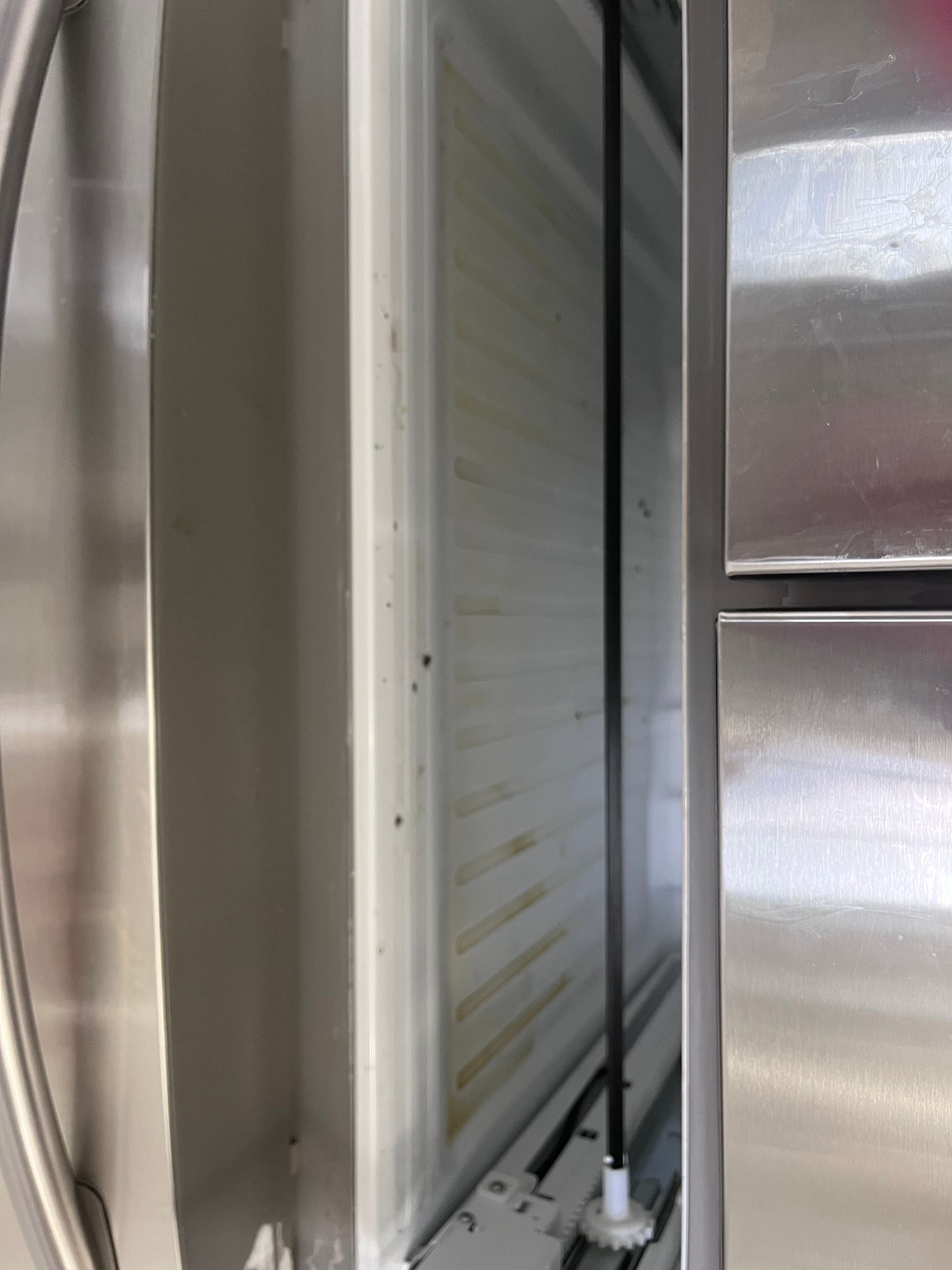 Interior of a white industrial refrigerator. A long black rod runs vertically down the center.