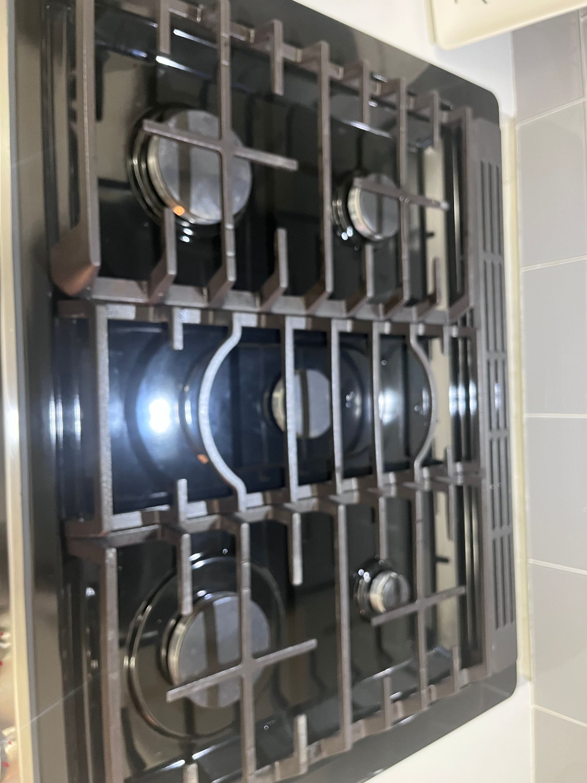 A black gas cooktop with four burners and a dark gray griddle. The grates and burner knobs are visible.
