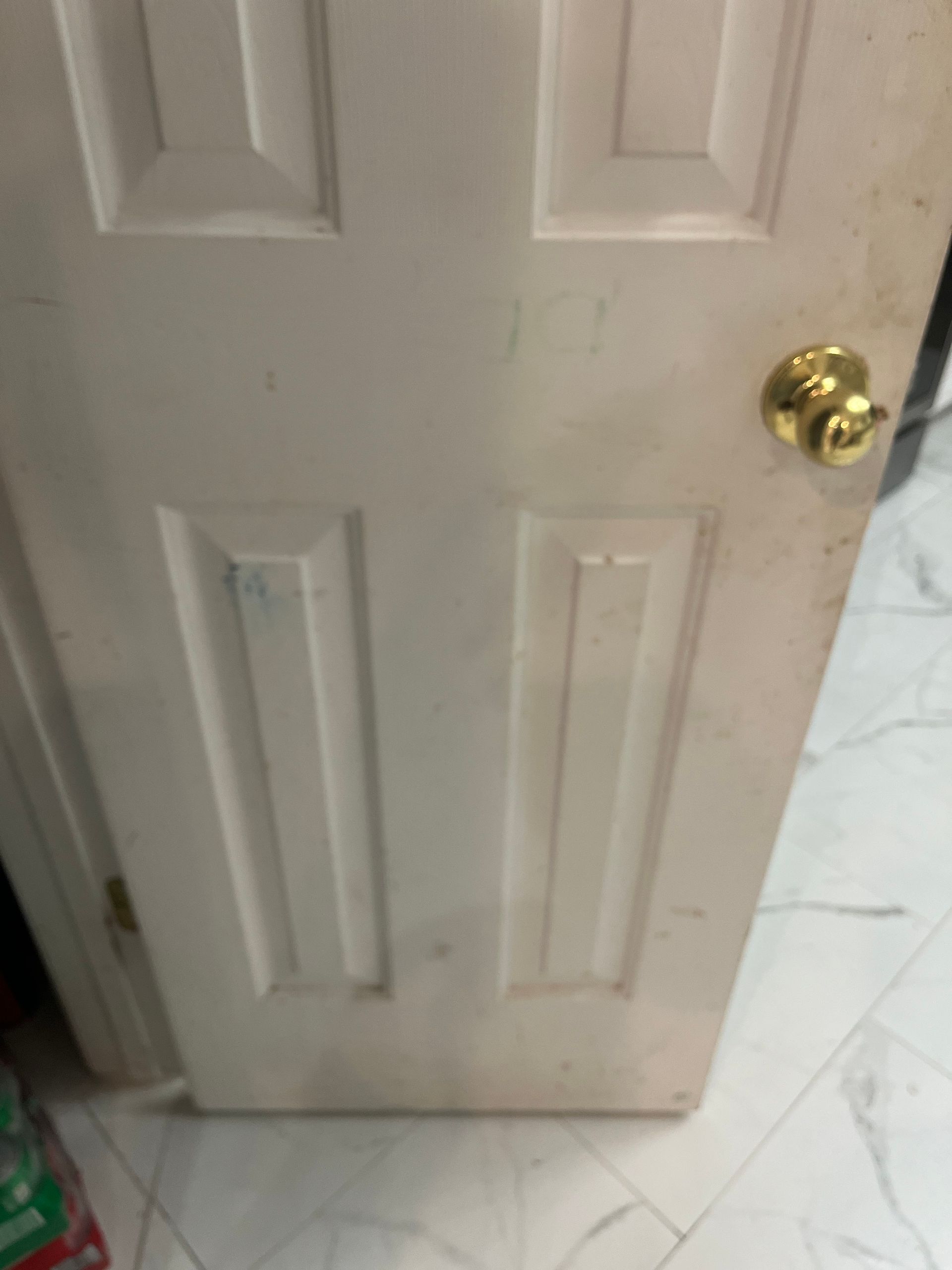 White interior door with gold doorknob, showing signs of wear, set on a tiled floor.
