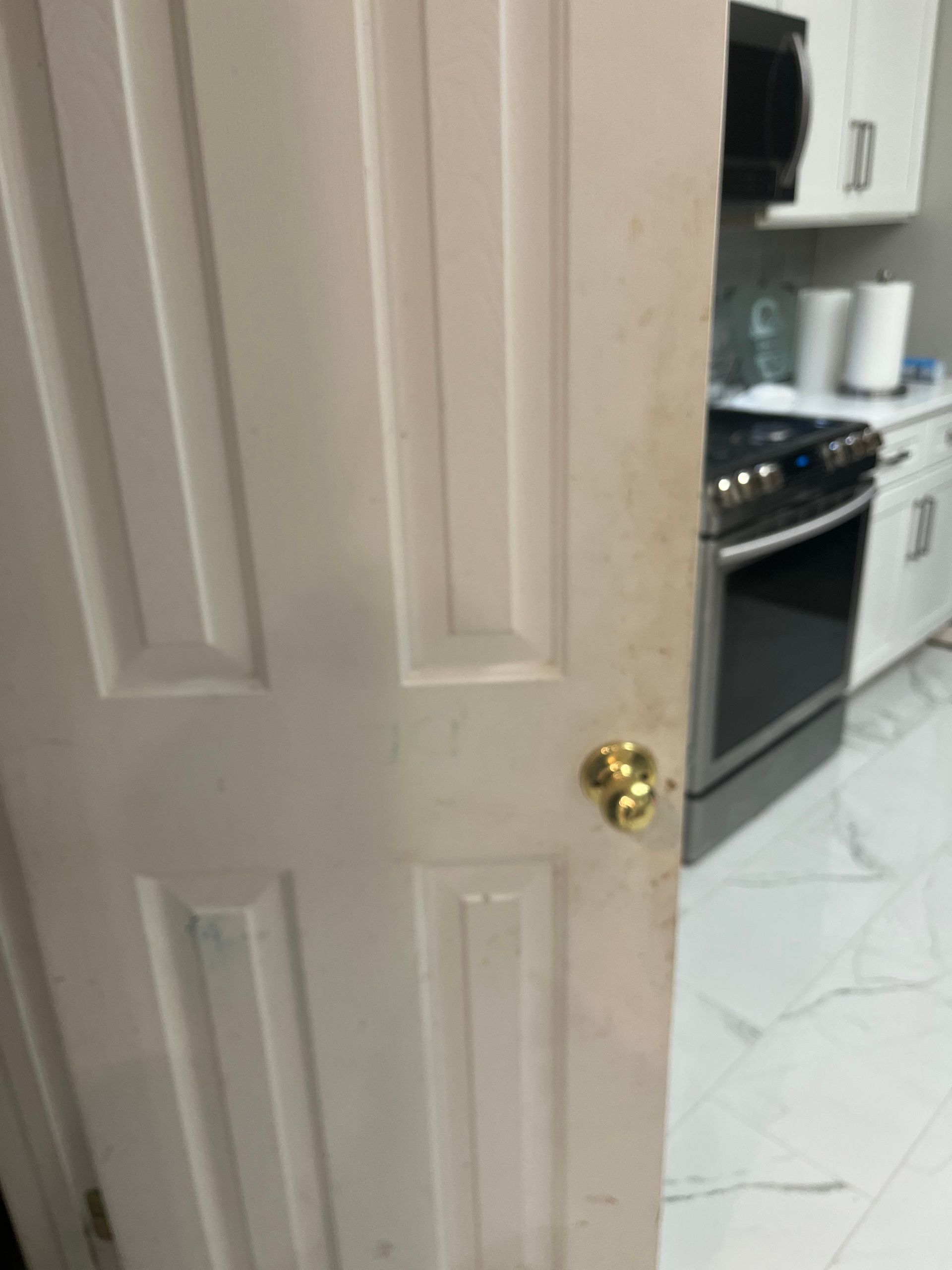 White door slightly ajar, revealing a kitchen with a stove, cabinets, and a roll of paper towels.