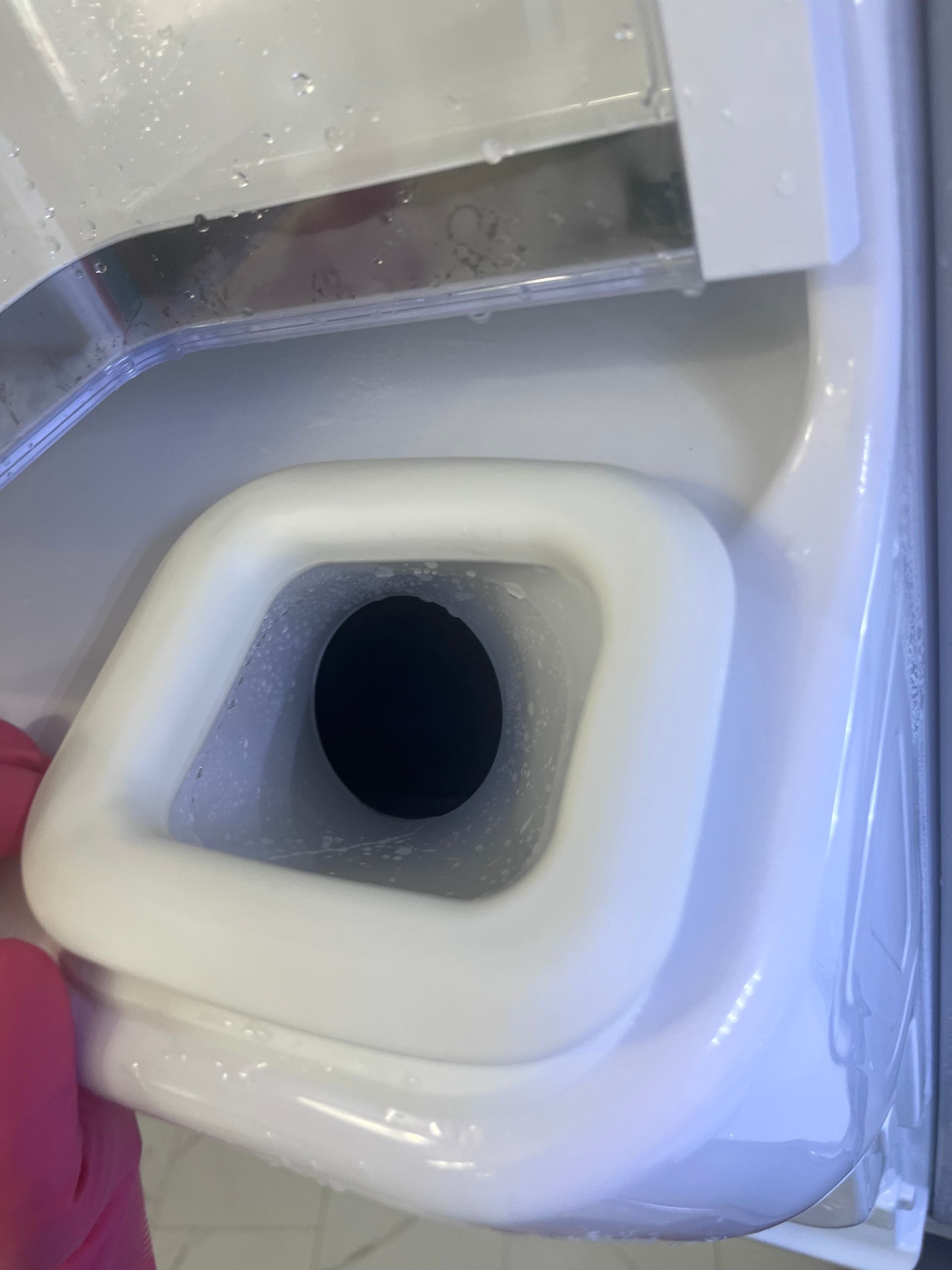 Close-up of a white rectangular drain opening on a white appliance. Inside the opening is a dark hole.