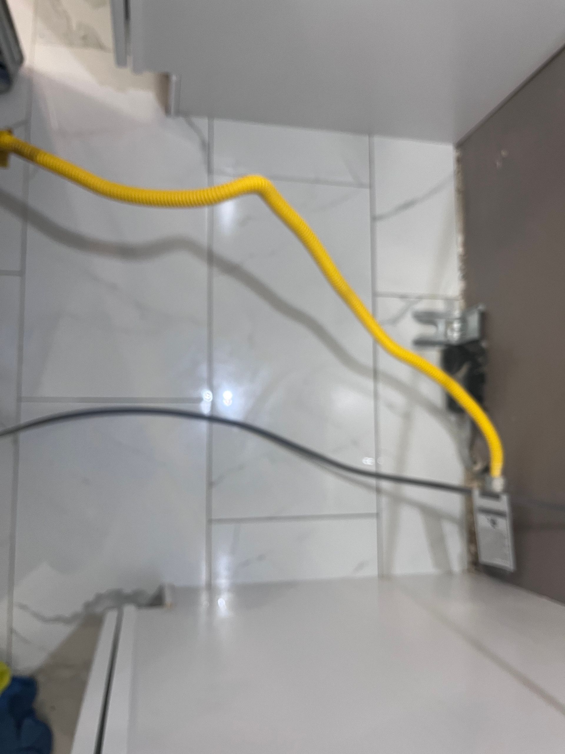 Yellow gas line snaking across white tiled wall, connected to a gas meter near a cabinet.