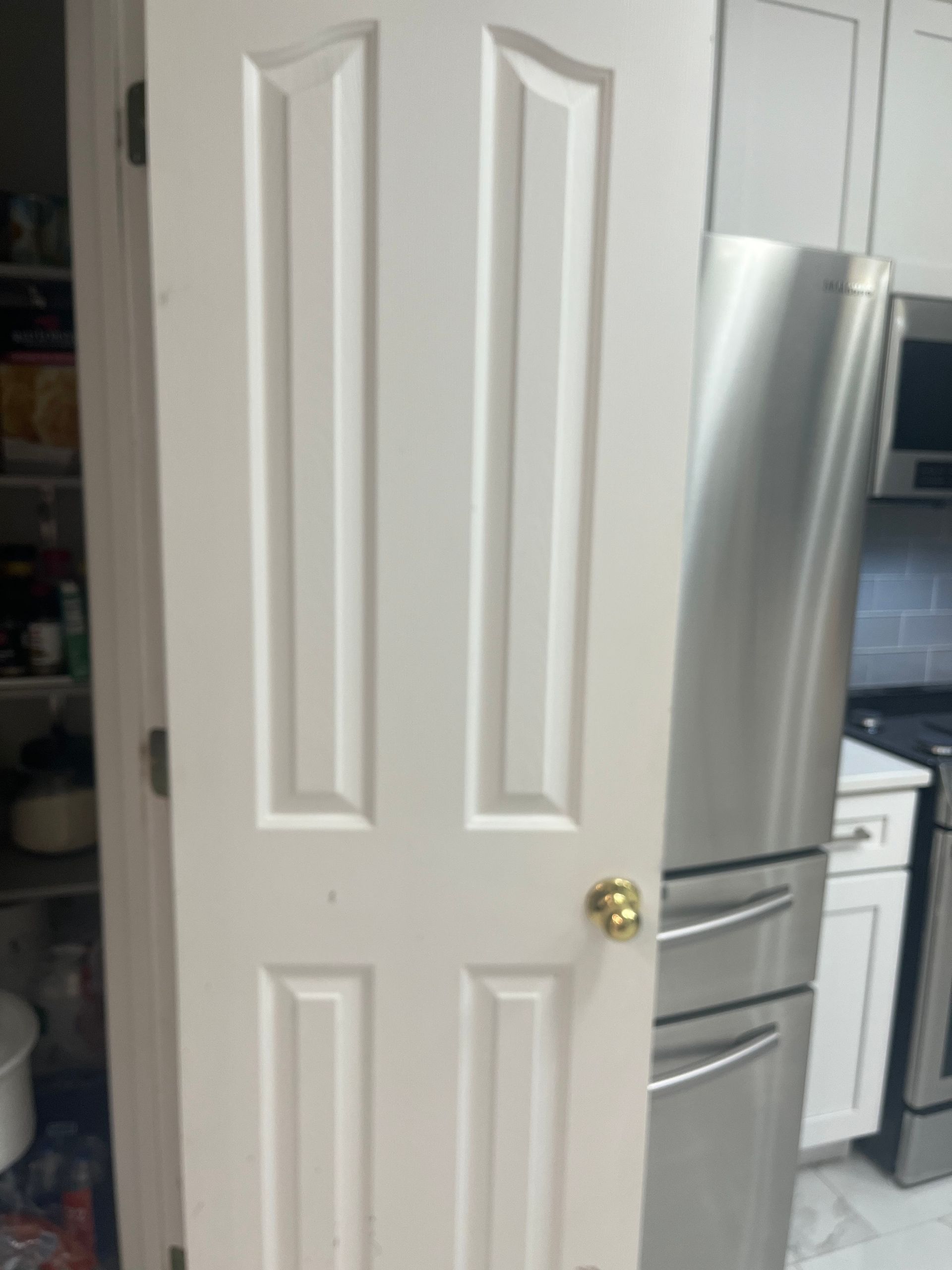 A white, four-panelled door in a kitchen setting; a stainless steel refrigerator is visible.