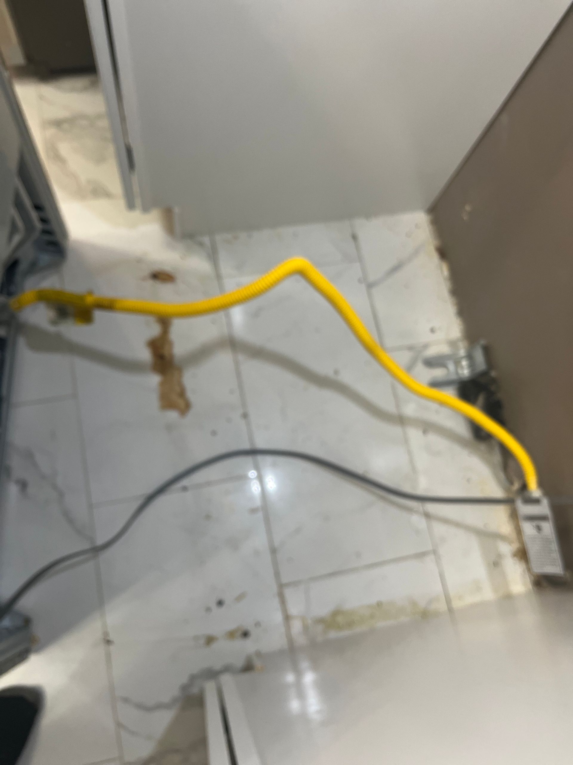 Yellow gas line and black cord on a white tiled floor, near what appears to be a stove and cabinetry.