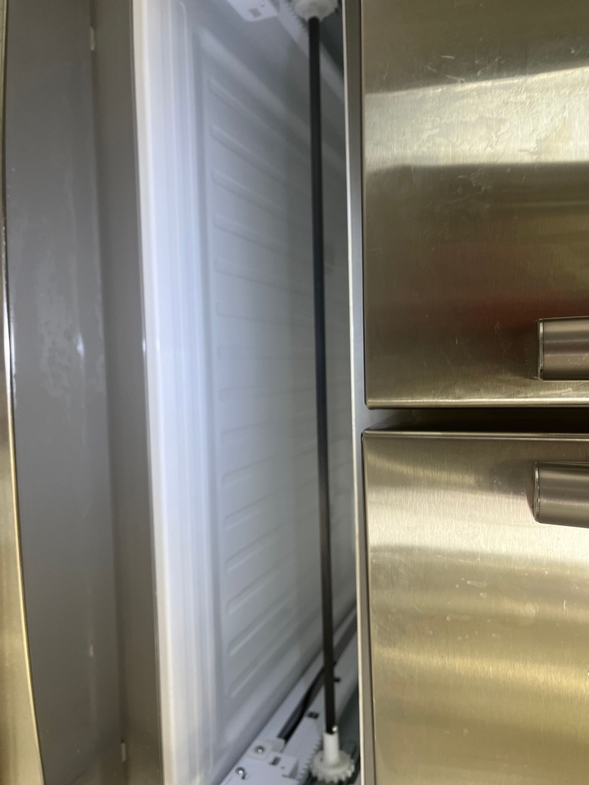 Inside view of a refrigerator with a long black rod and frozen white interior. Stainless steel doors are to the right.