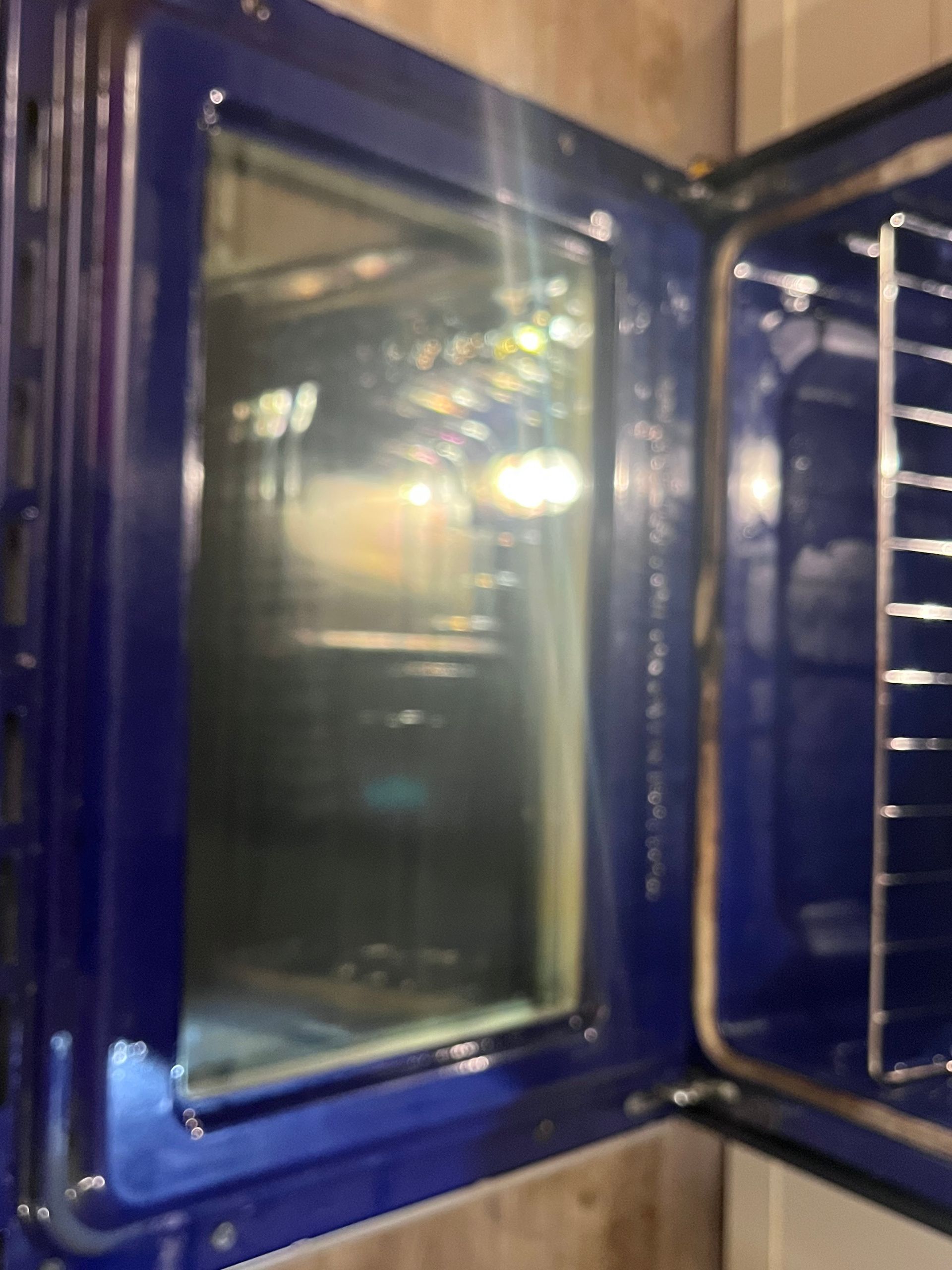 A partially open oven, showing the interior with a blue enamel interior and glass door. The oven rack is visible.