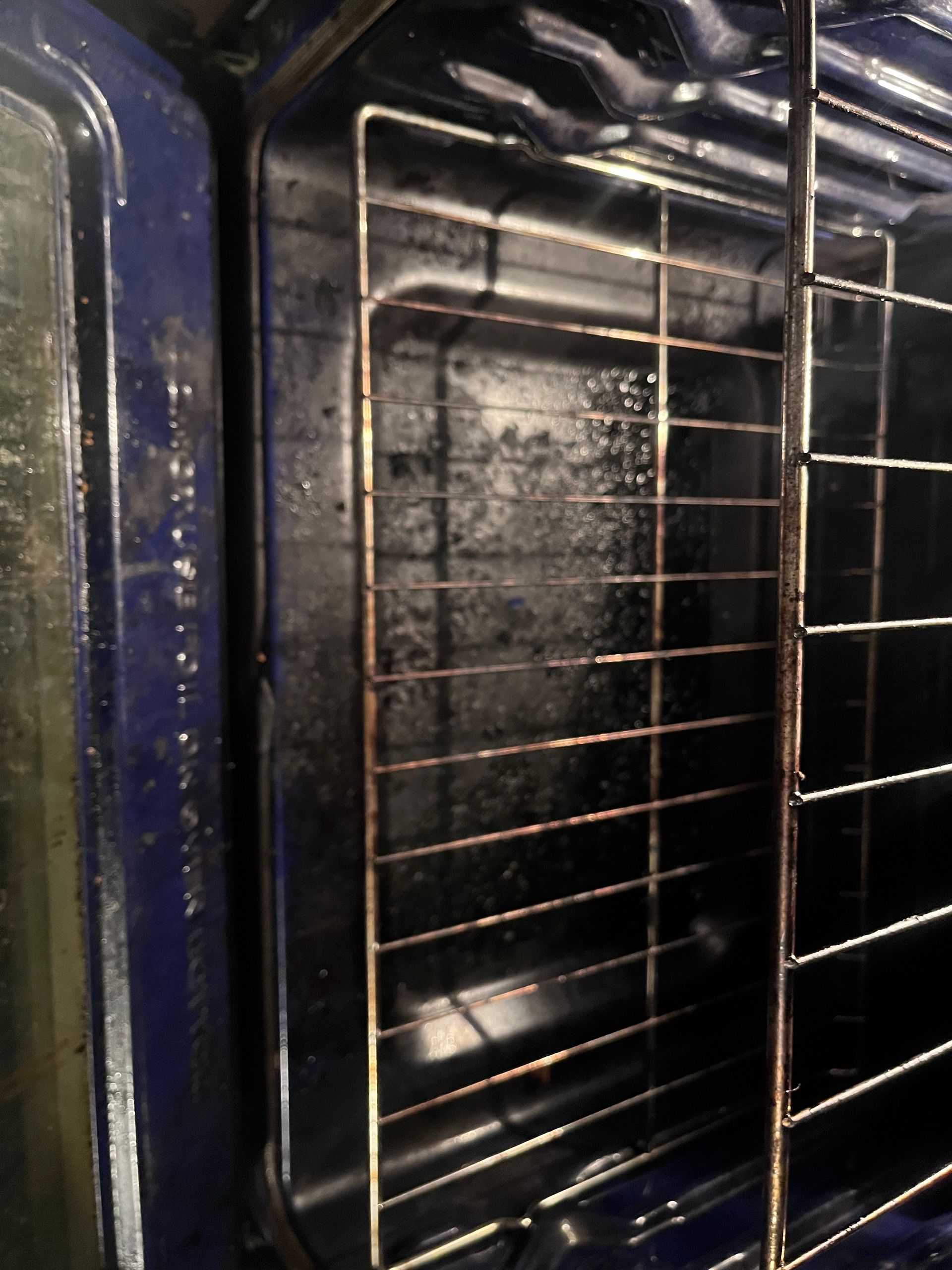 Inside of an oven with a rack, showing baked-on food residue on the sides and floor, and a dark blue interior.