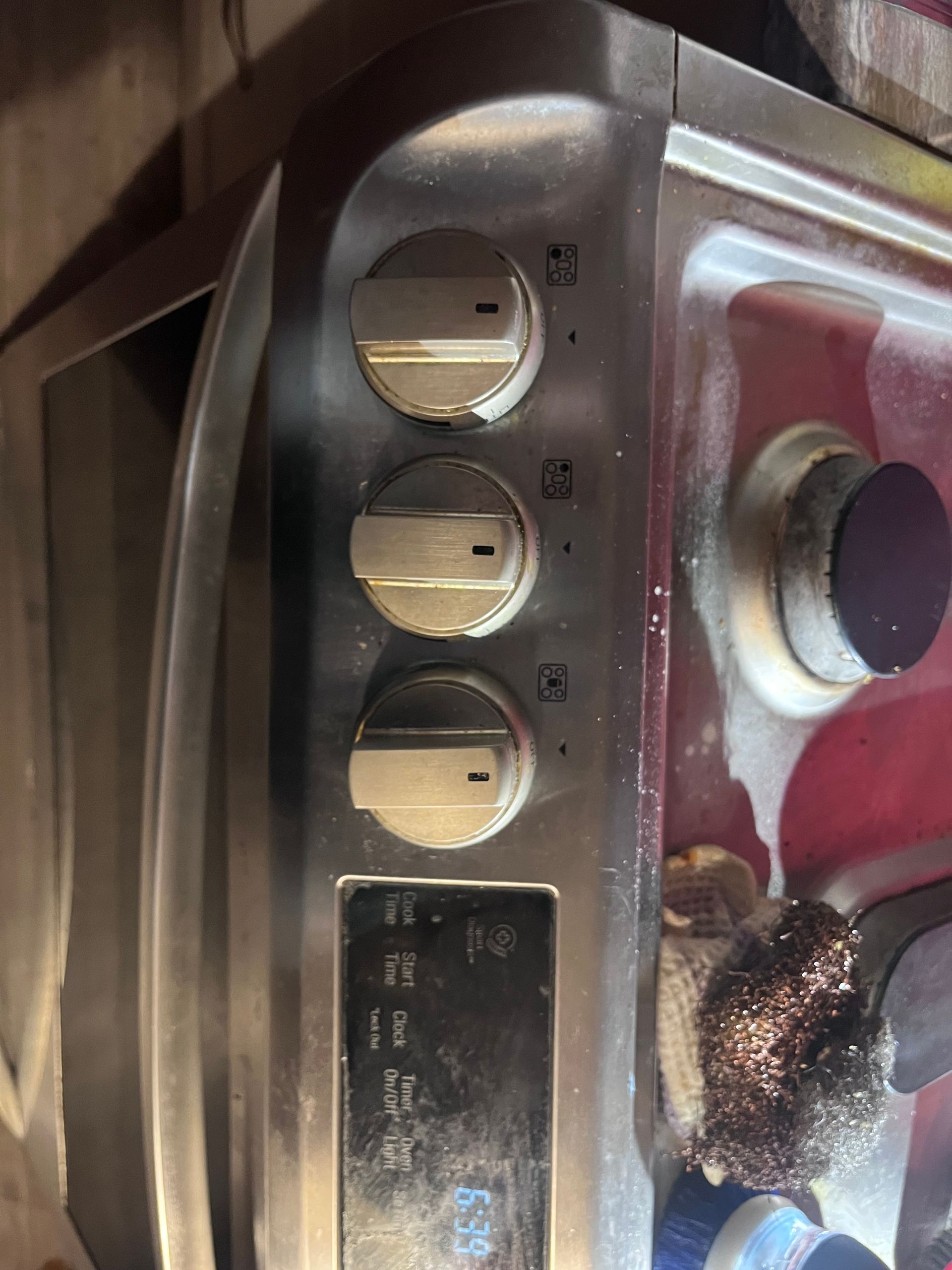 Close-up of a stainless steel stove control panel with three dials and a digital display.