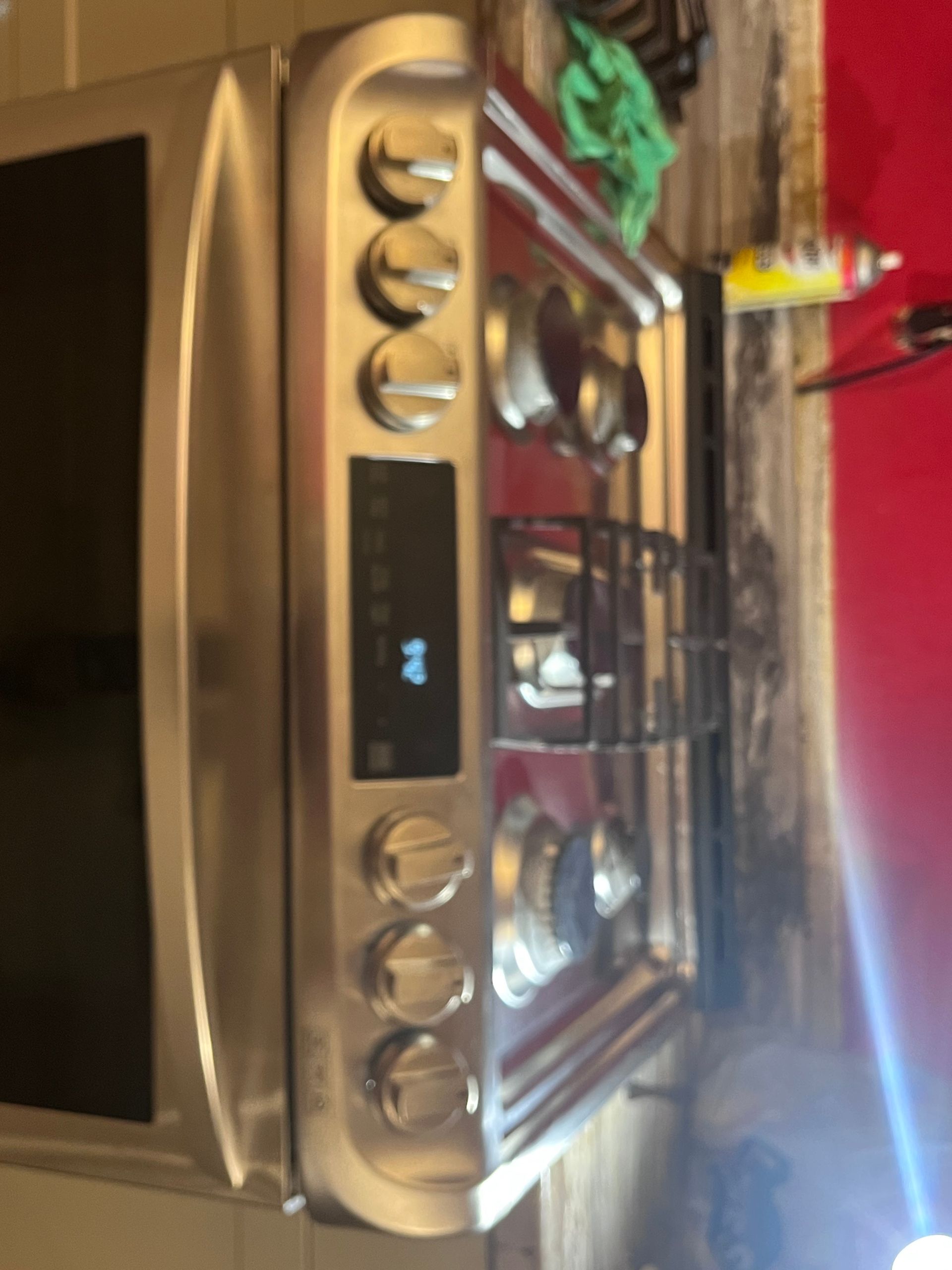 A stainless steel gas range with a black glass cooktop and control panel displaying a digital readout.