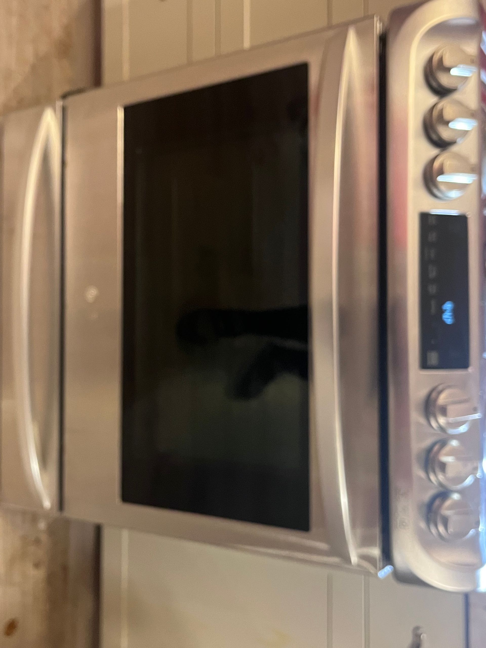 Stainless steel oven with black glass door and control panel with dials and display.