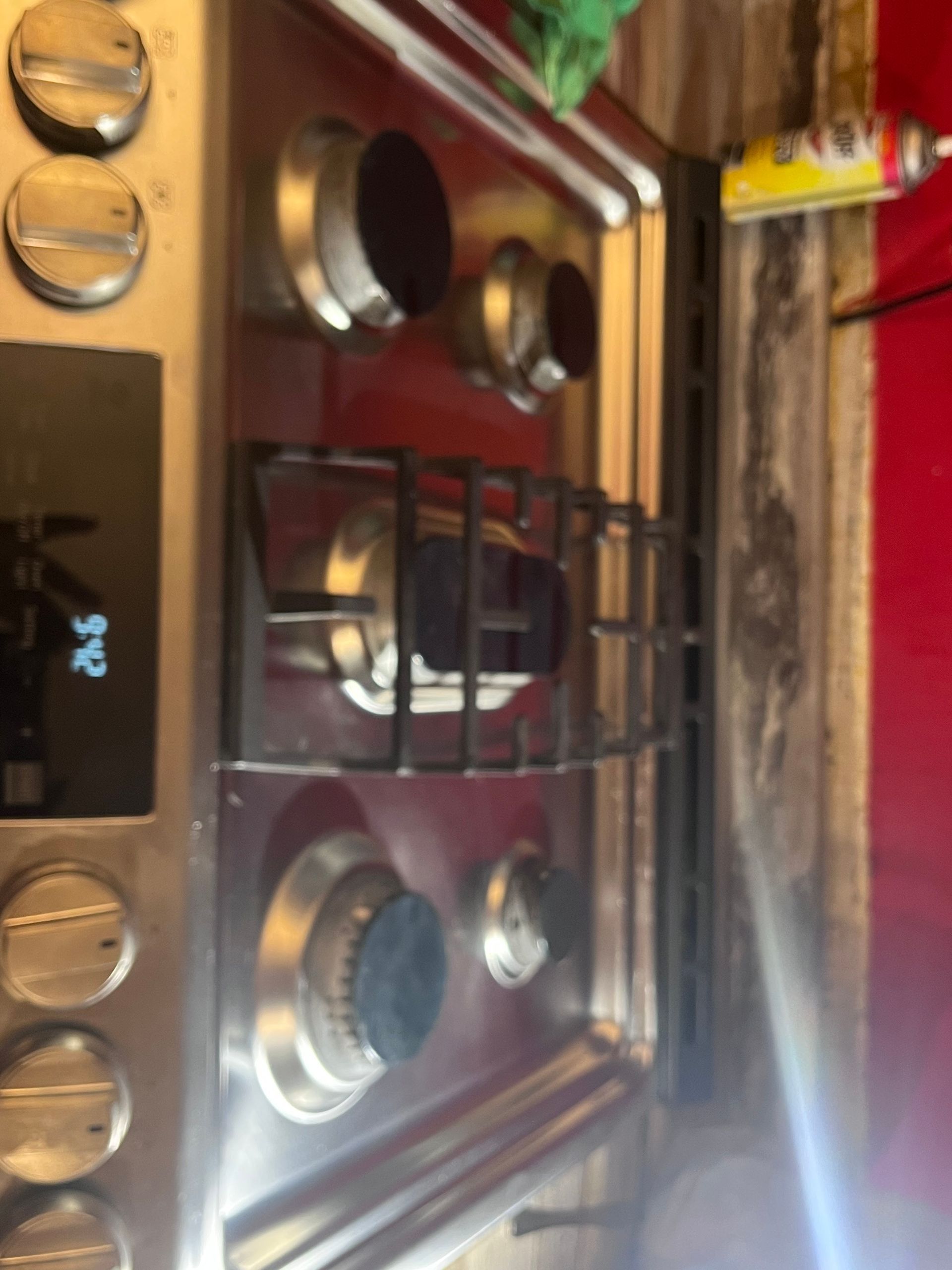 A stainless steel gas stovetop with five burners and knobs, viewed from above. A digital display shows 