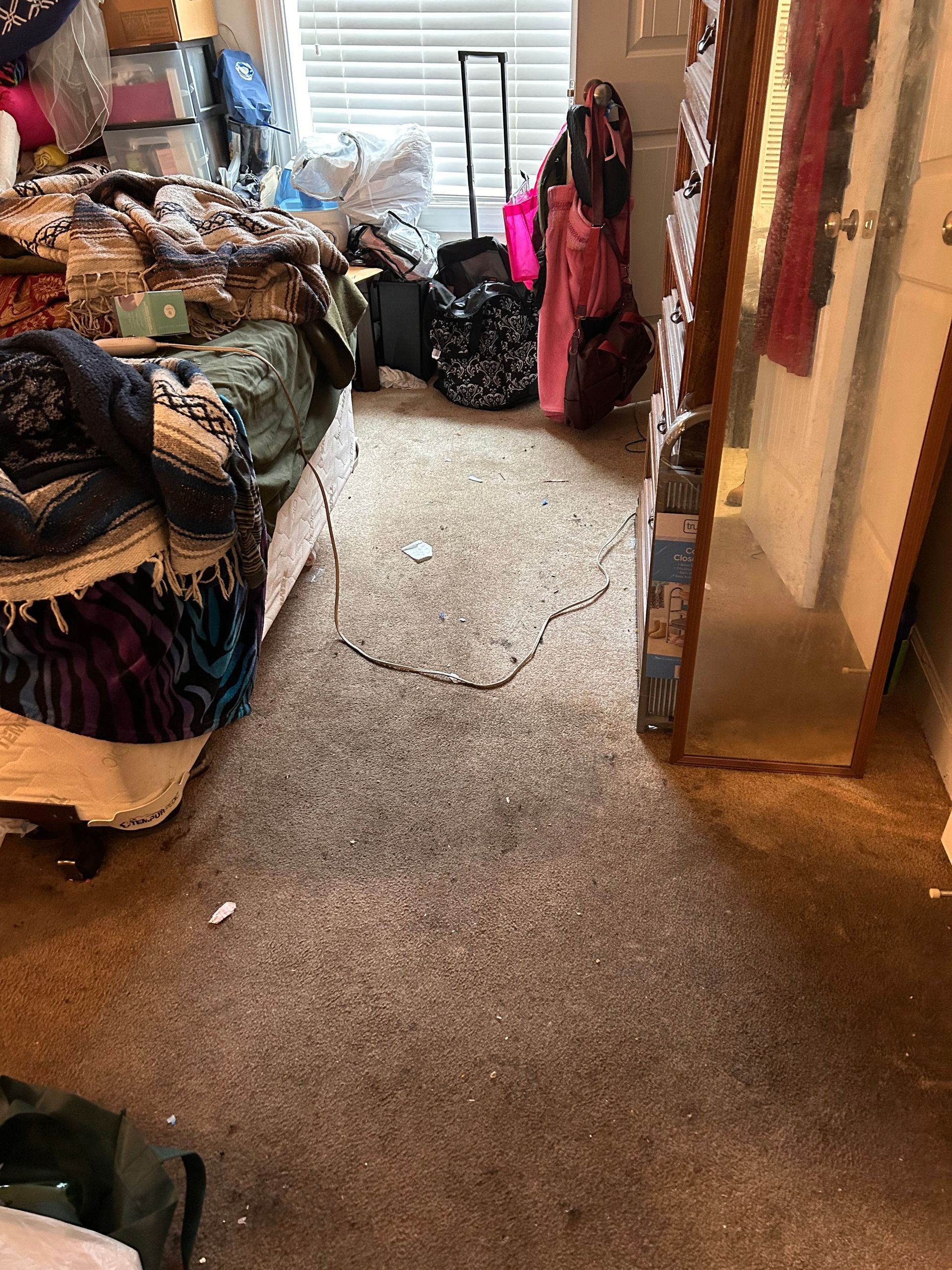 A cluttered room with piles of belongings. A narrow path is clear in the center, leading toward a full-length mirror.