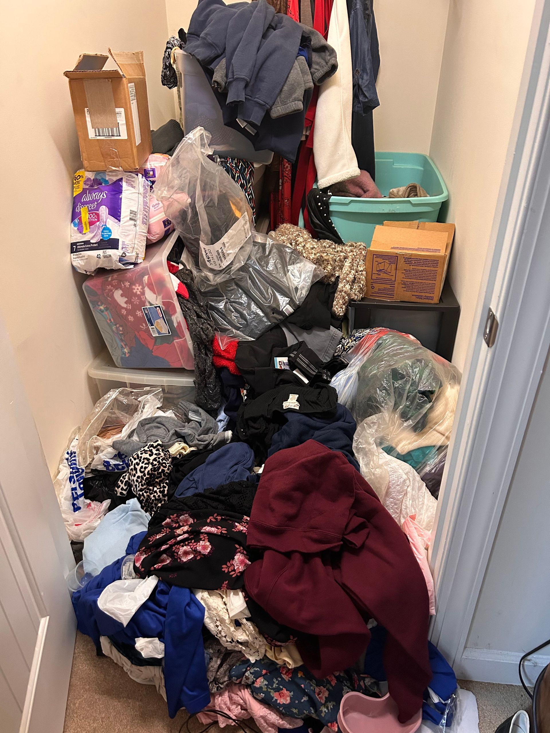 Messy closet overflowing with clothes, boxes, and a storage bin. The items are a mix of colors and textures.