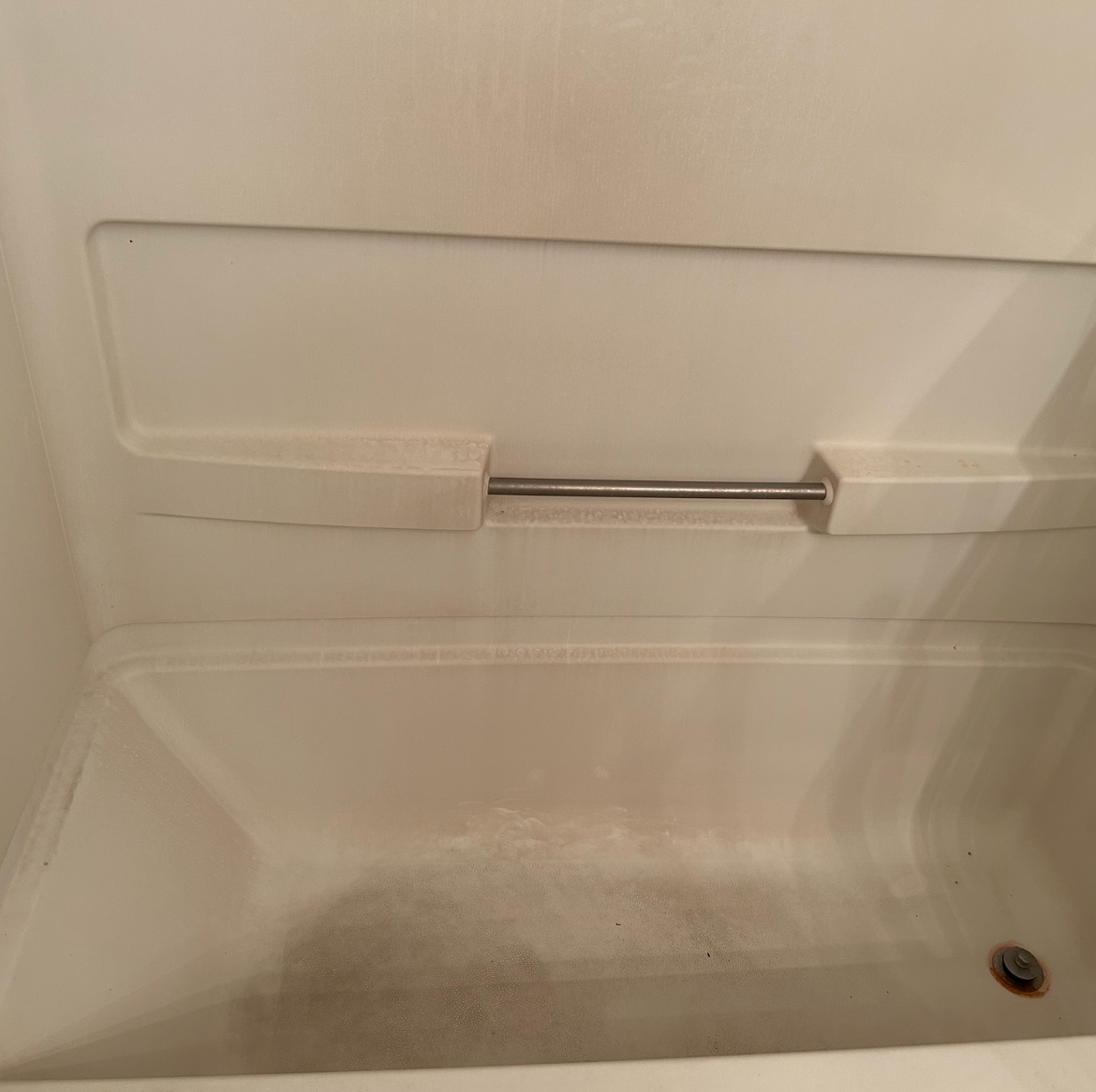 An empty, off-white bathtub with a built-in ledge and a metal towel bar. The tub shows signs of use.