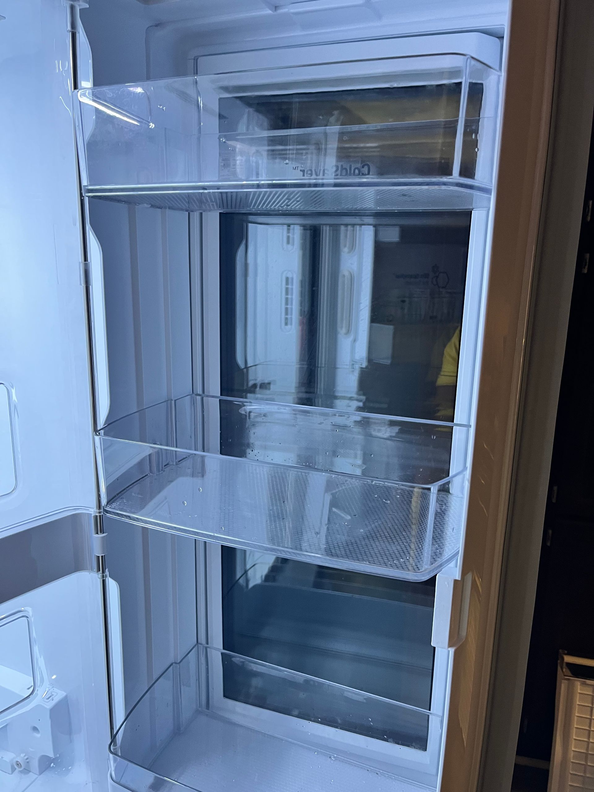 Empty, open refrigerator interior with clear plastic shelves.