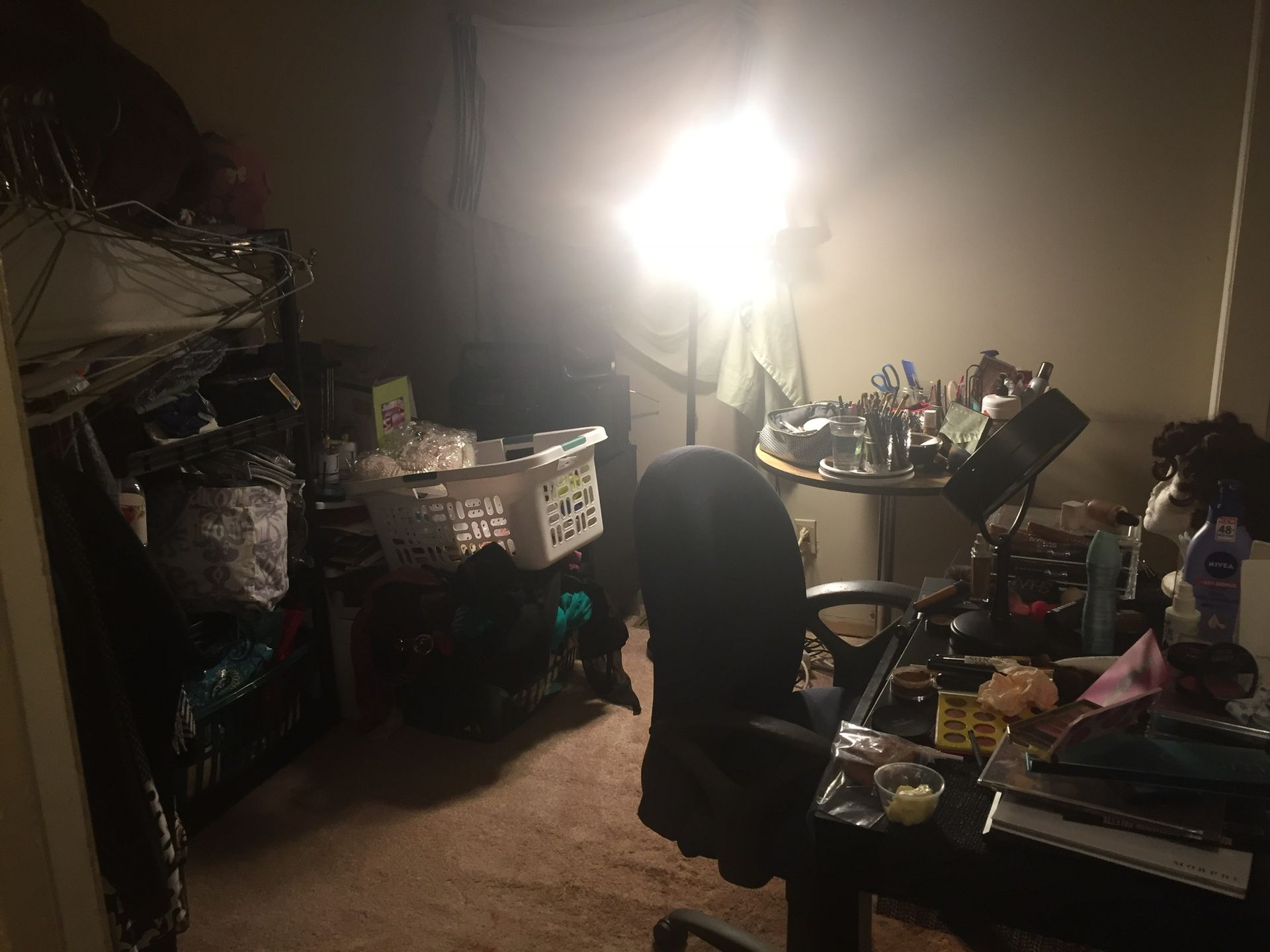 Cluttered room with a desk, chair, and shelves holding various items. A bright light illuminates the scene.