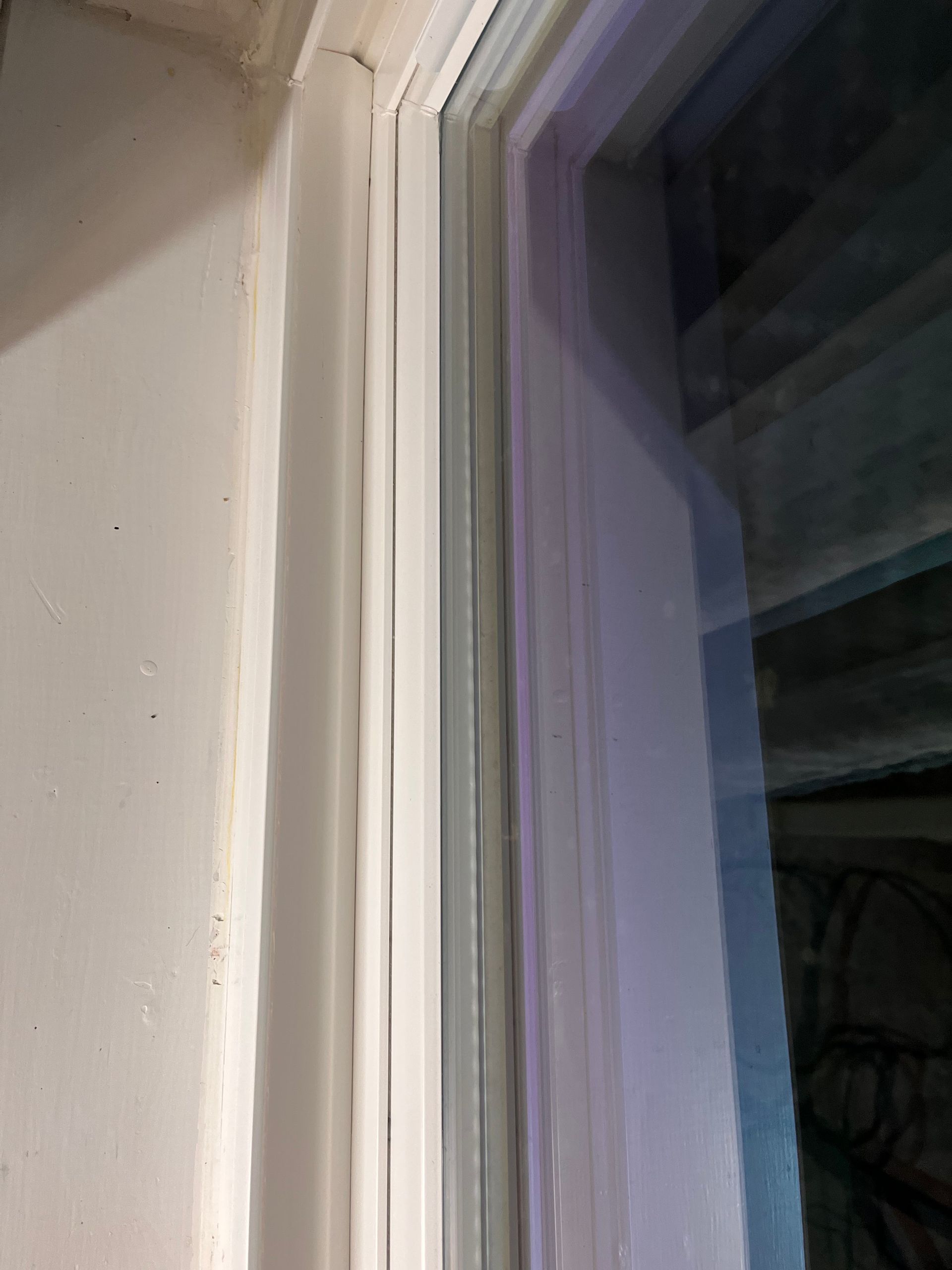 Close-up of a white window frame with glass panes, showing the edge of the window and wall.