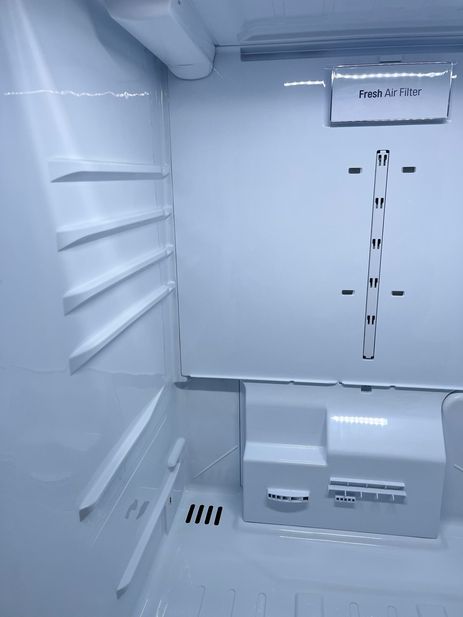An empty, white refrigerator interior. Shows shelves, compartments, and a built-in dispenser.