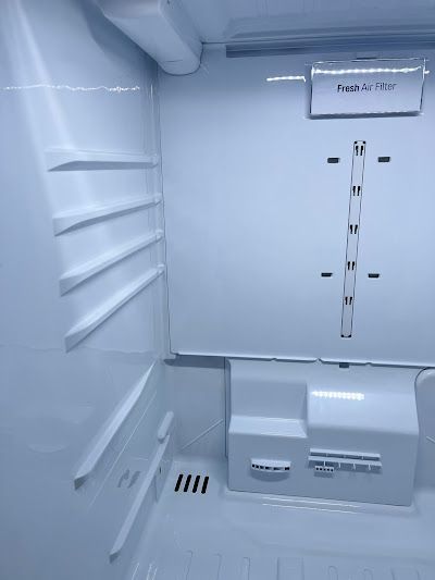Empty refrigerator interior with adjustable shelves, air filter, and built-in dispenser. White and gray tones.