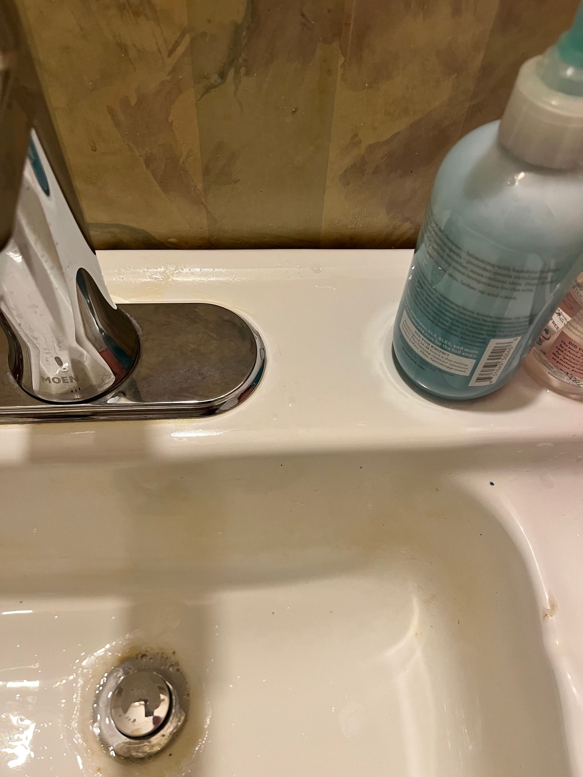 White bathroom sink with chrome faucet, a blue bottle, and a slightly dirty surface.