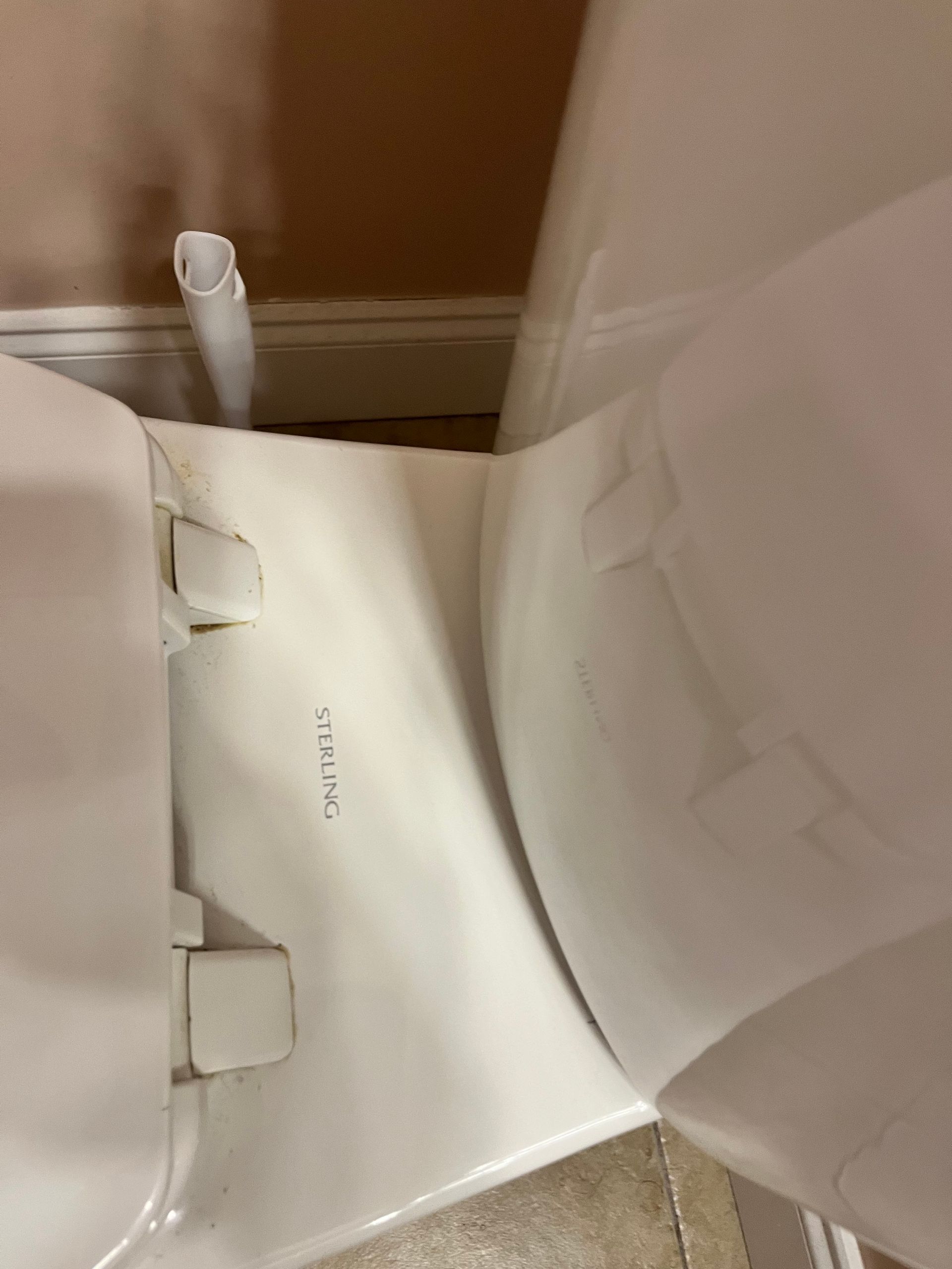 White toilet seat and bowl, viewed from above and to the side. The seat is up, and a white brush is behind the toilet.