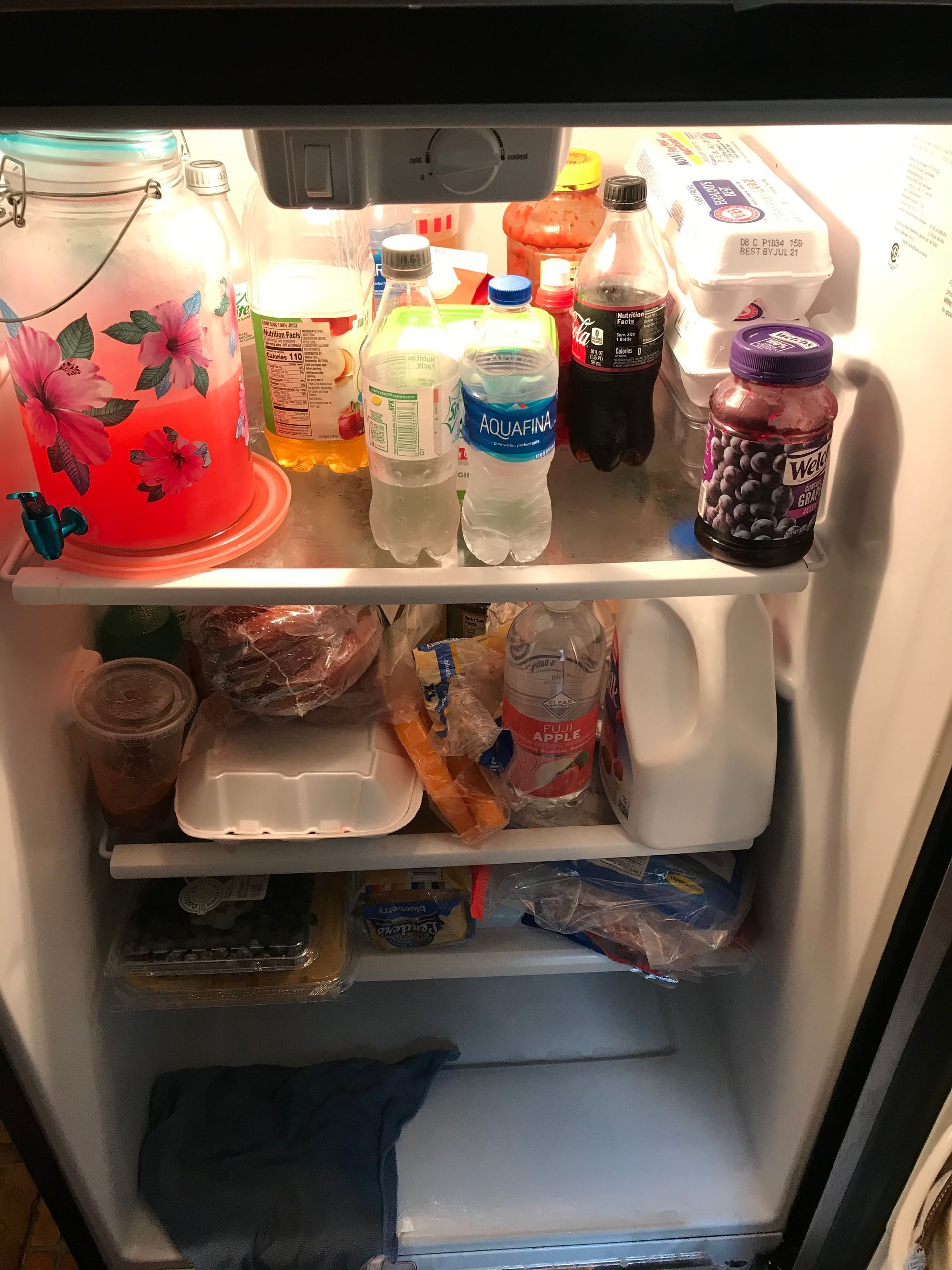 A refrigerator interior illuminated by a light, showcasing various food items and drinks stored on shelves.
