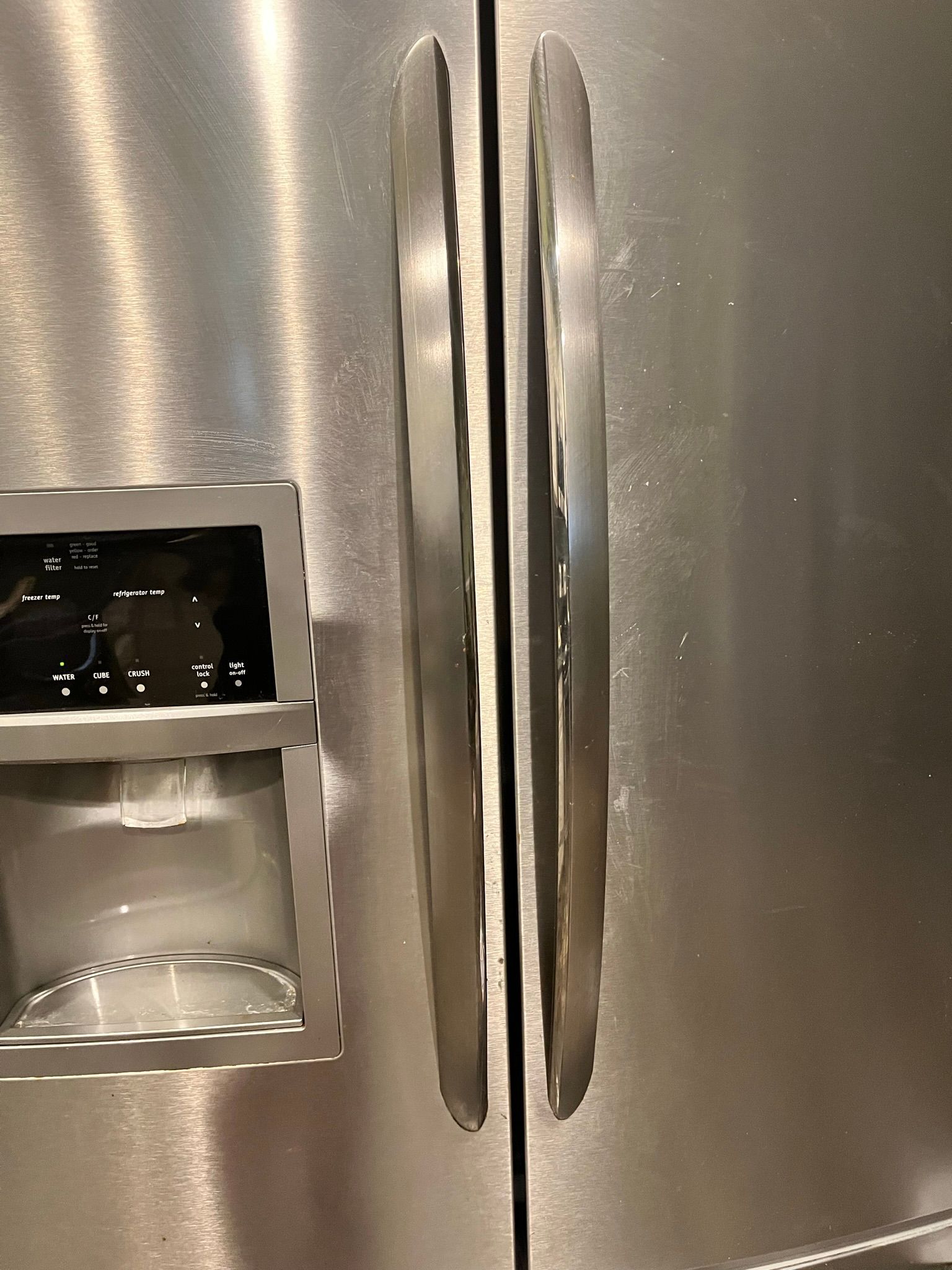 Stainless steel refrigerator with two vertical door handles, a water dispenser, and ice maker on the left door.