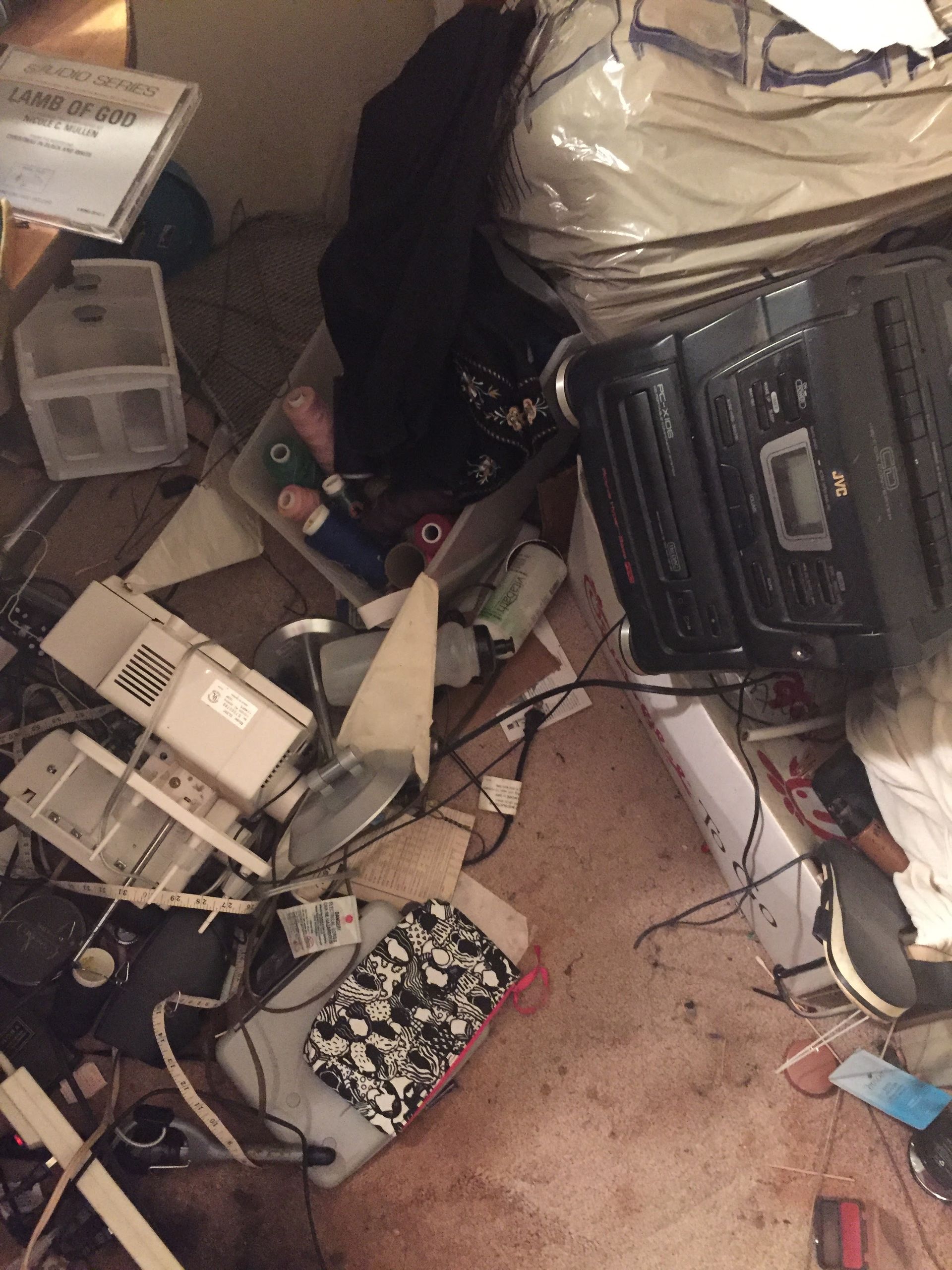 Cluttered room with electronics, boxes, and debris scattered on the floor. Various wires and items are piled haphazardly.