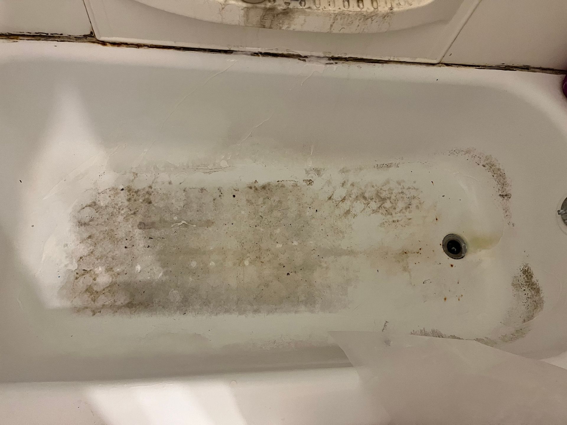A dirty bathtub with dark stains, likely mold or mildew, on the bottom and edges.