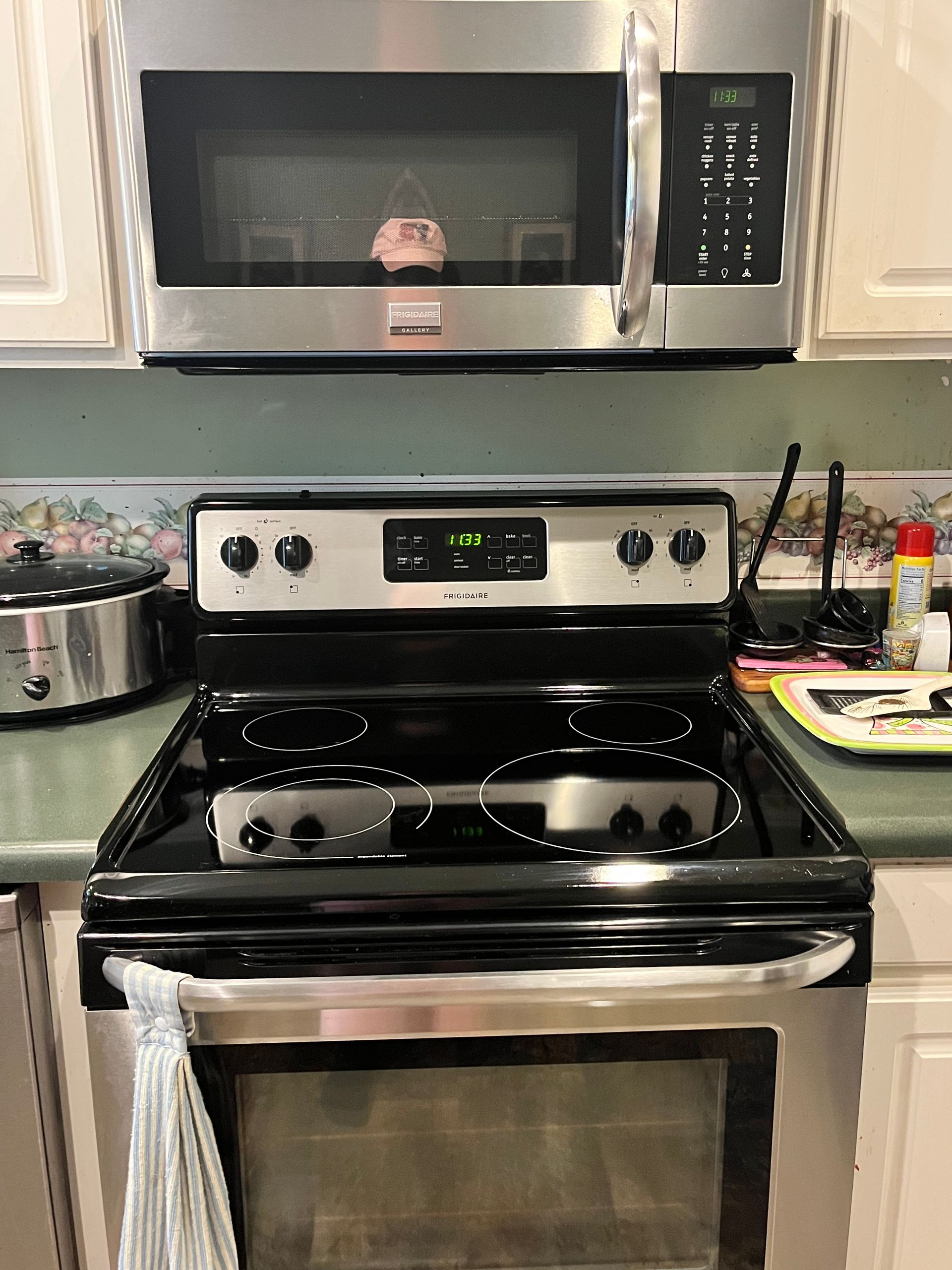A kitchen scene with a stainless steel microwave above a black electric range. A slow cooker sits to the left.