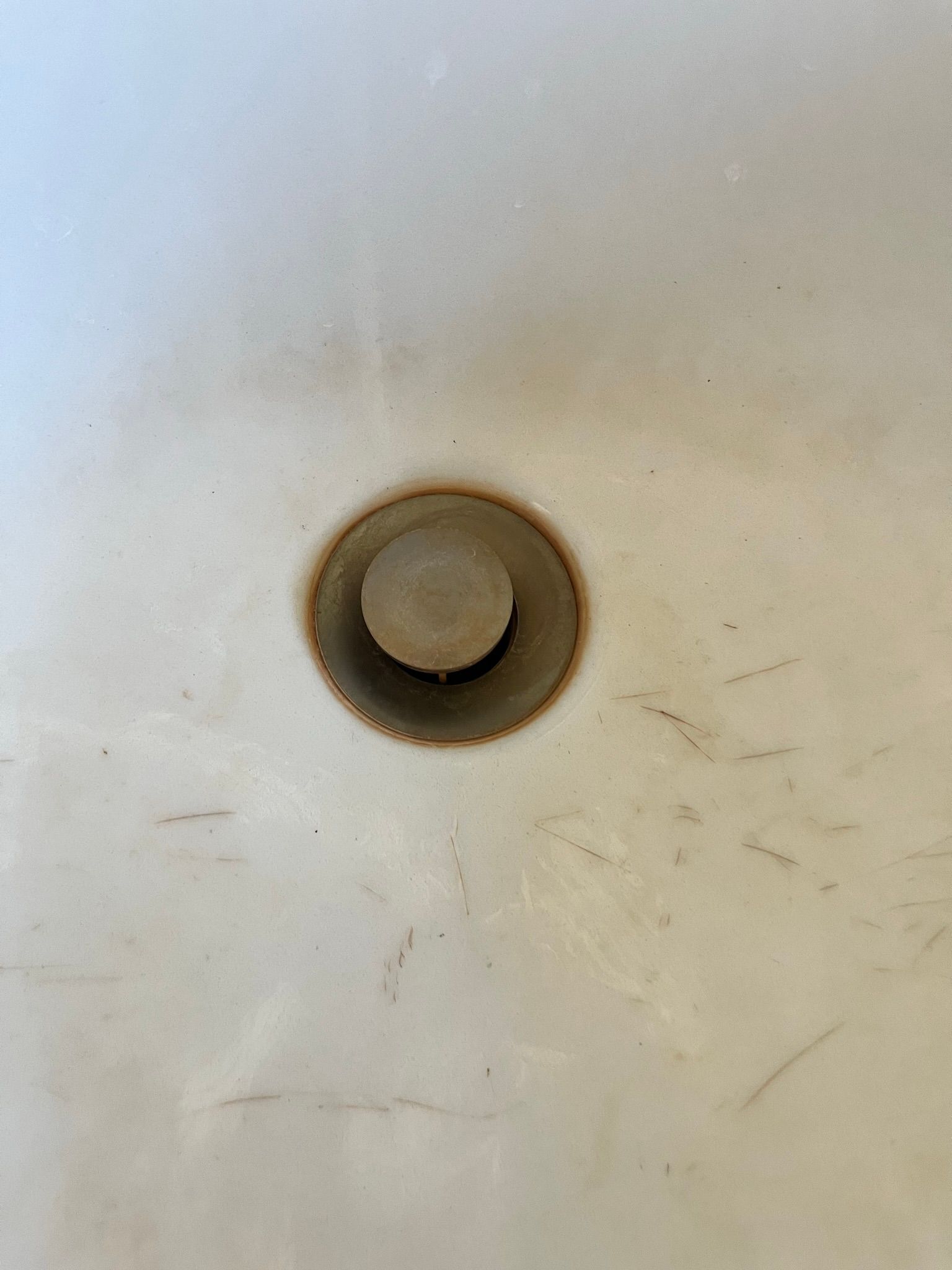 Close-up of a bathtub drain with a round, rusty-looking drain cover. The tub has dirt marks around the drain.
