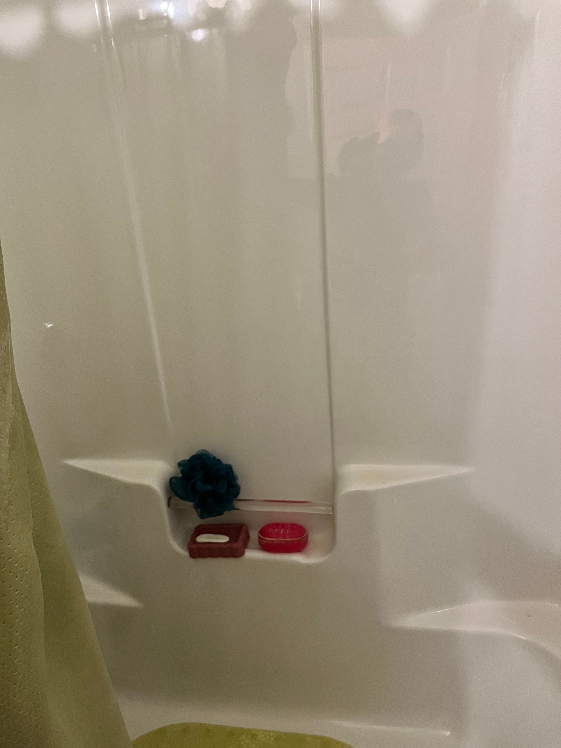 A shower stall with a built-in shelf holding soap and a blue sponge. A green towel hangs on the left.