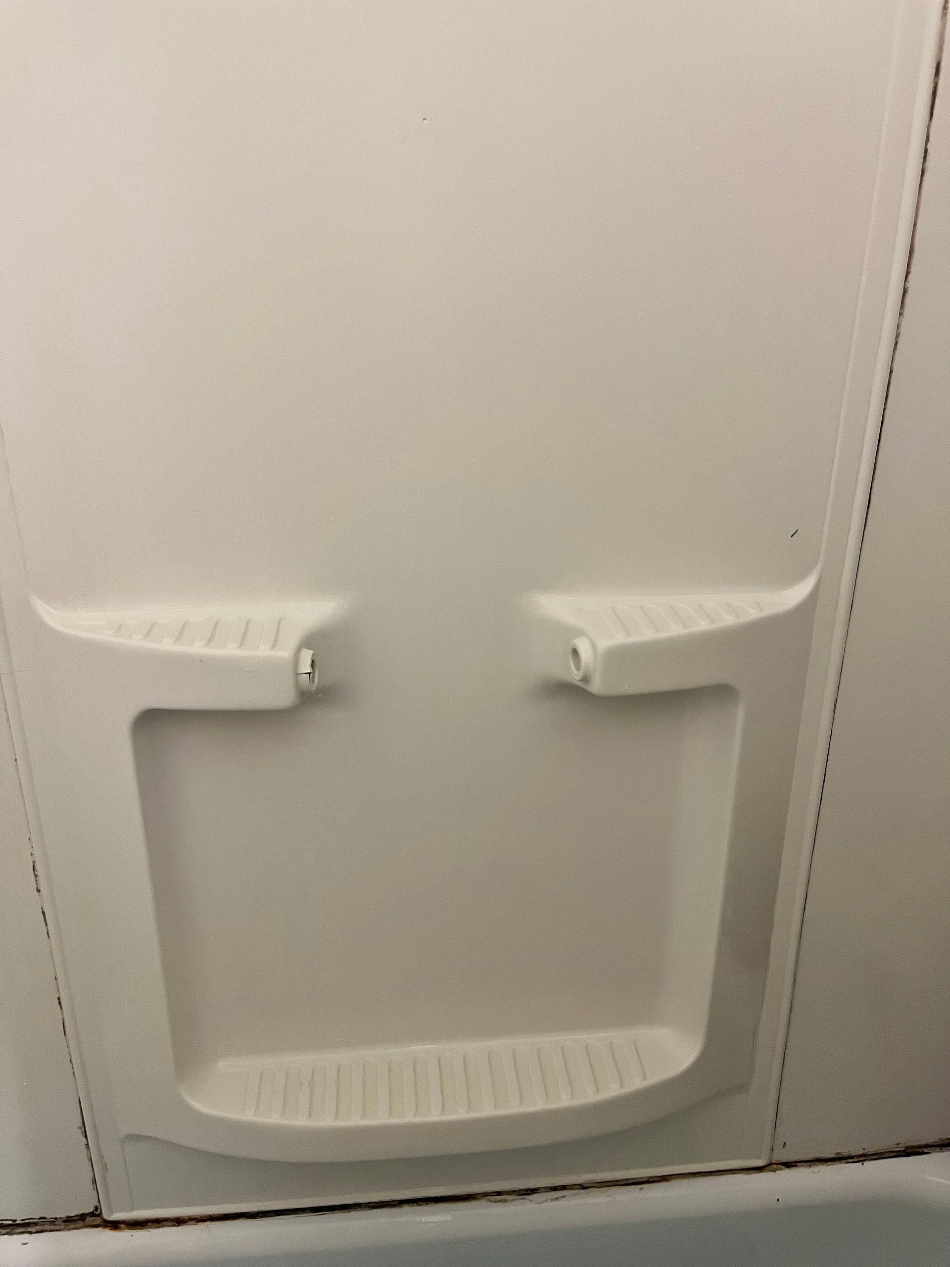 White molded plastic shower wall with built-in soap dishes and a lower ledge above the tub.
