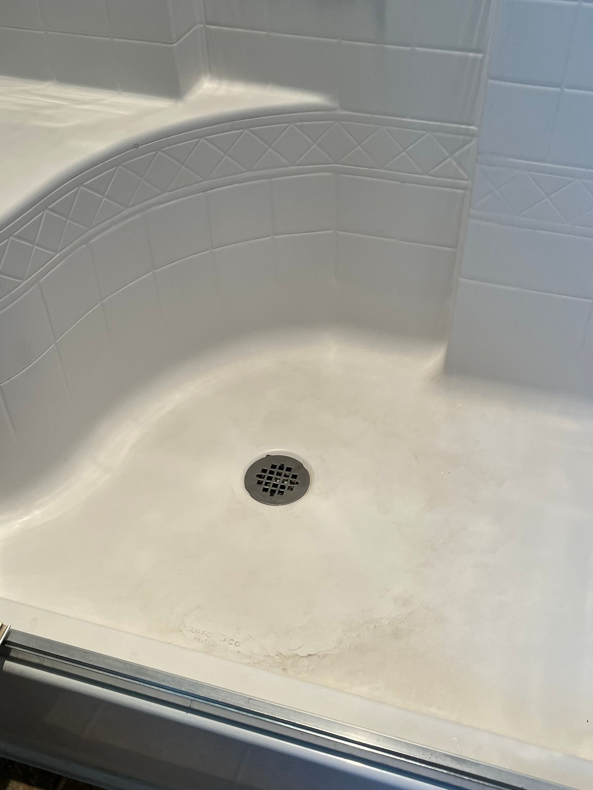 White, curved-corner shower stall with a drain. Mildew stains are visible at the bottom.