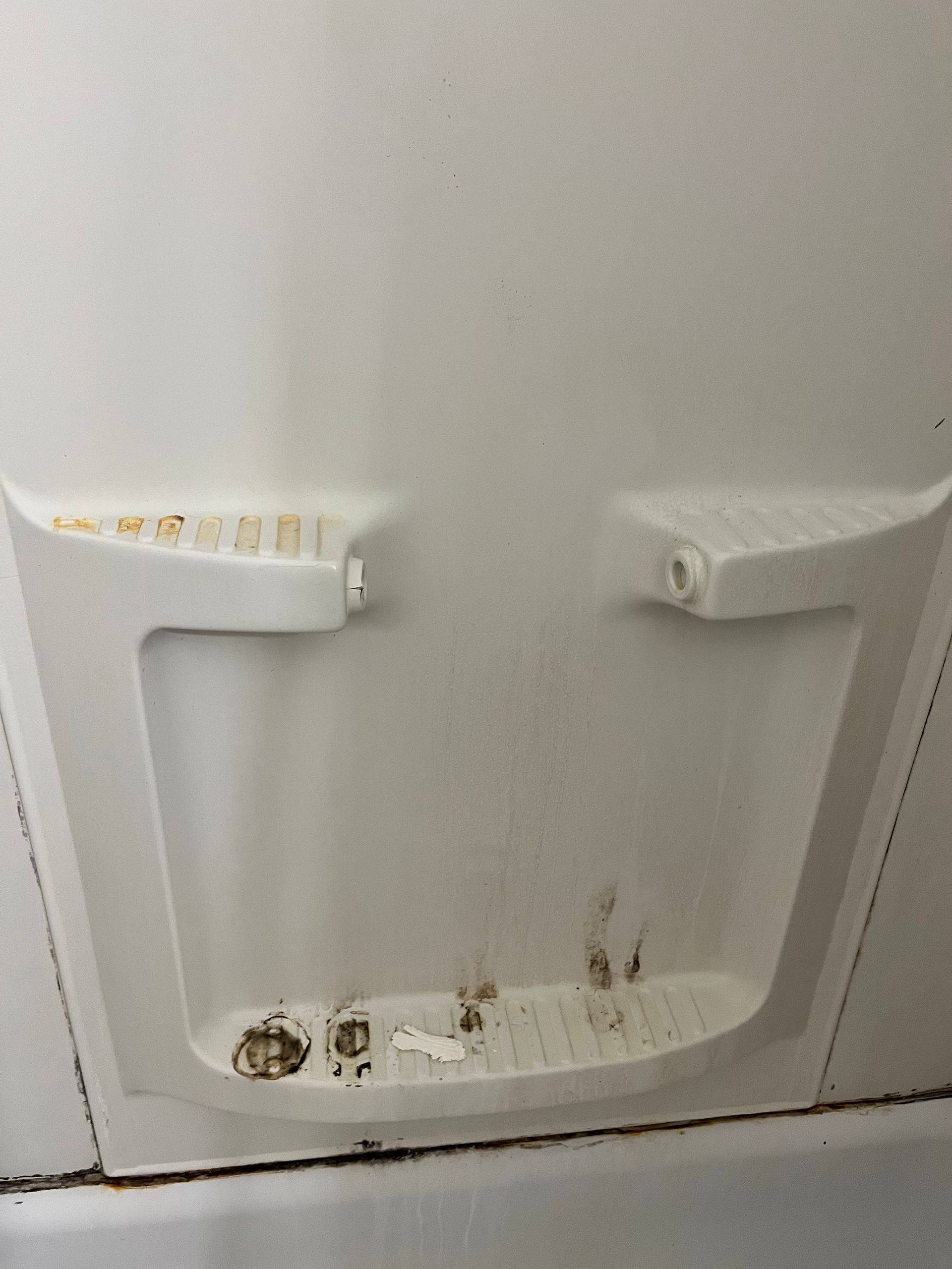 A dirty, white built-in shower unit with two shelves and visible mold and stains on the floor.