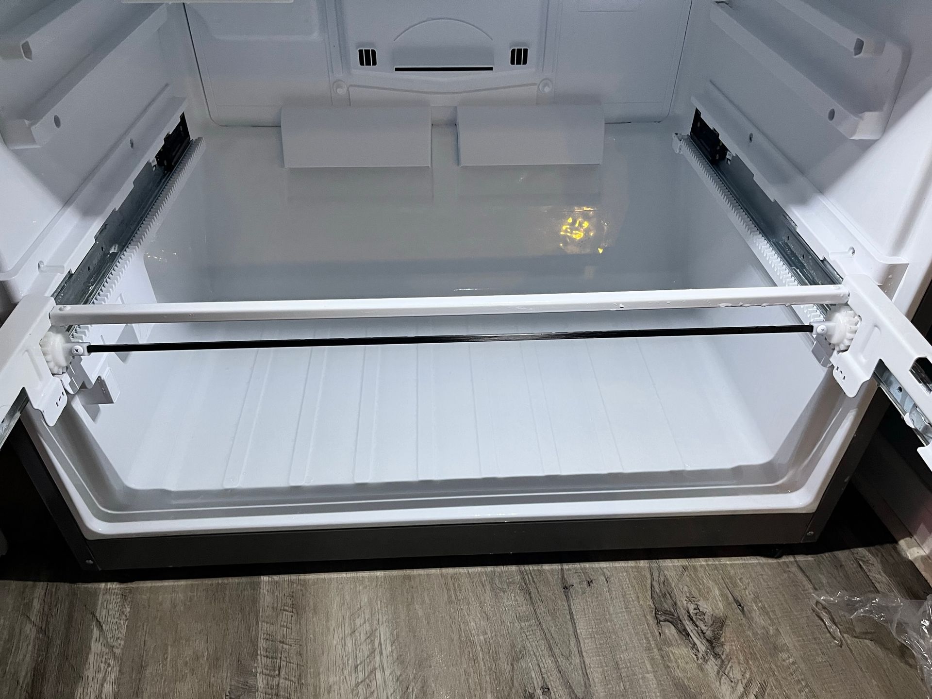 Empty white refrigerator interior, looking into the bottom drawer area. A horizontal bar is visible.