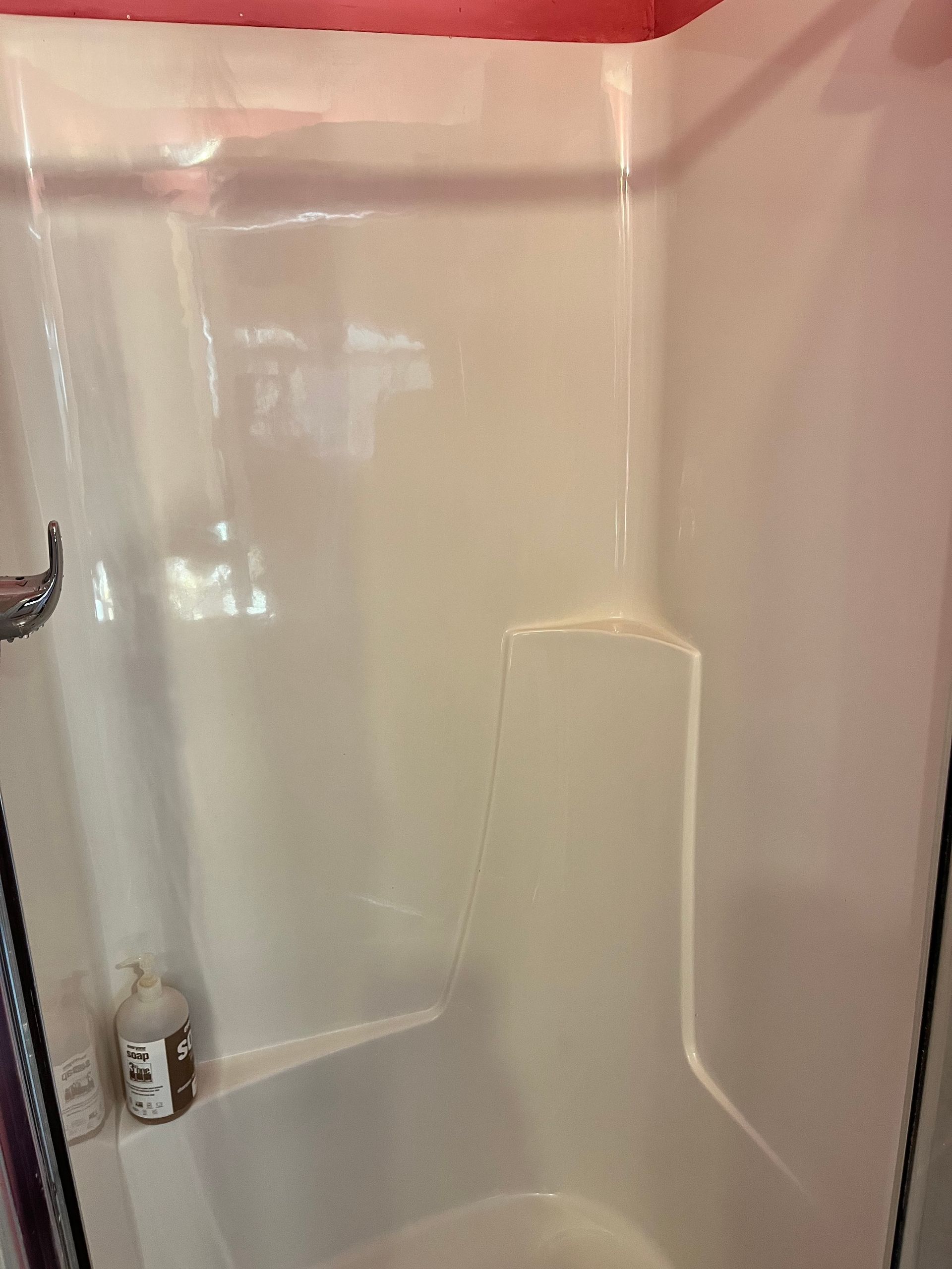 White plastic shower stall with a built-in shelf and a red painted ceiling. A bottle of soap is visible.