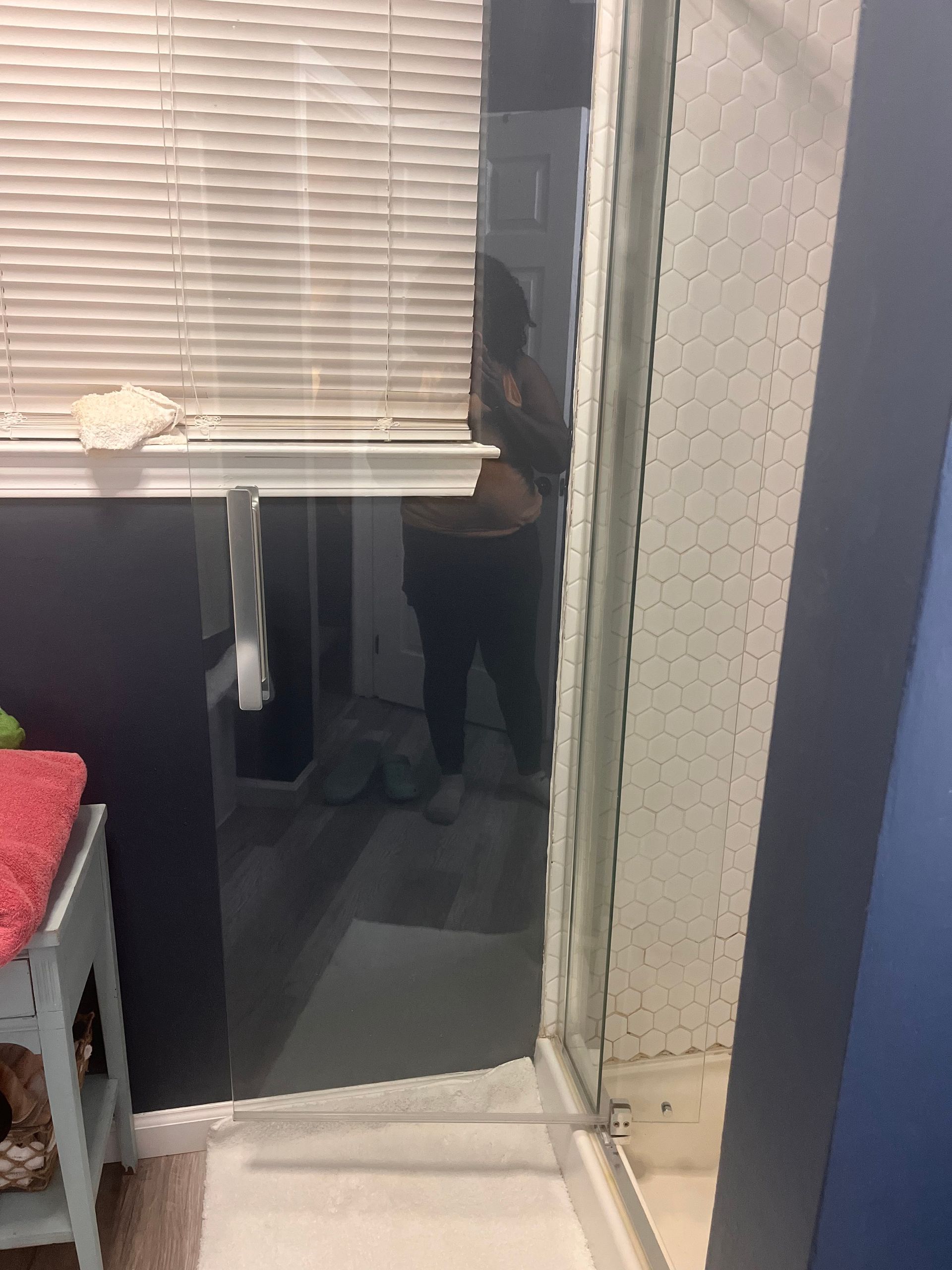 A person standing in front of a shower door is reflected in the glass. The person wears dark clothing.