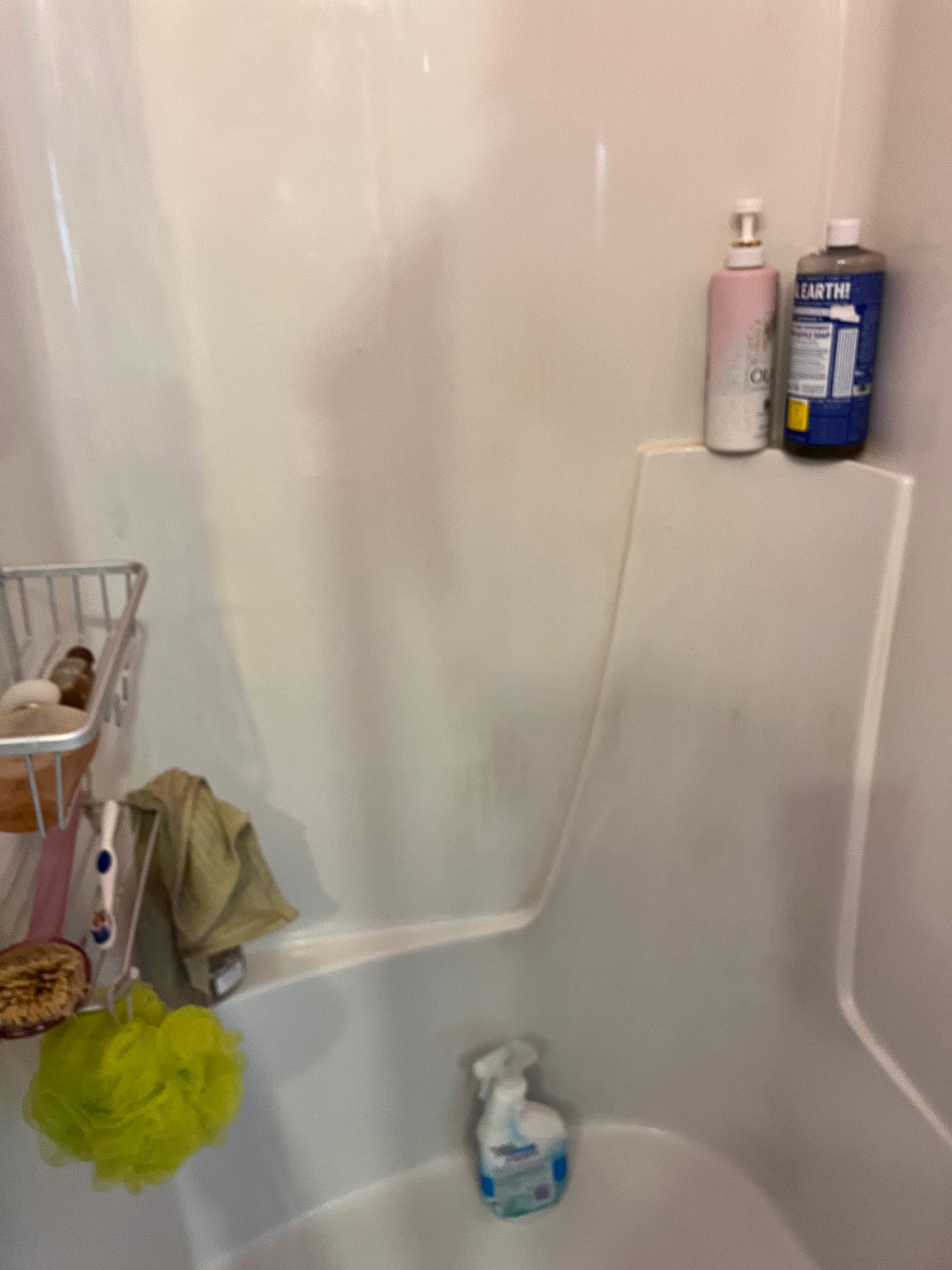 White shower interior with bottles of toiletries on a ledge. A sponge, washcloth, and caddy are also visible.