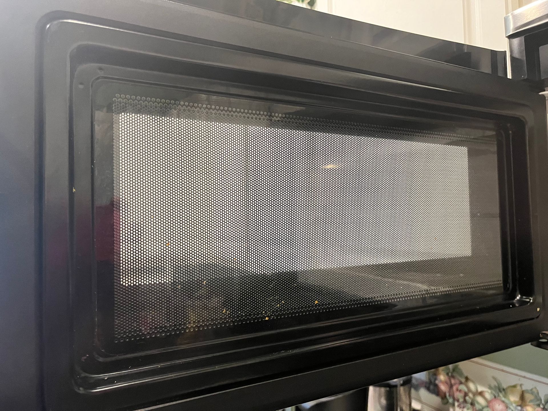Open black microwave, interior visible through the mesh screen, displaying an empty interior.