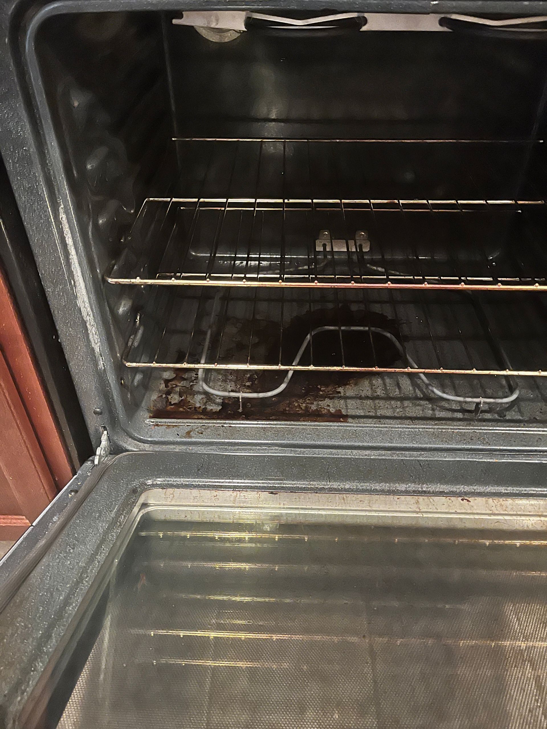 Dirty oven interior, dark with visible grease and food residue on the bottom and racks.