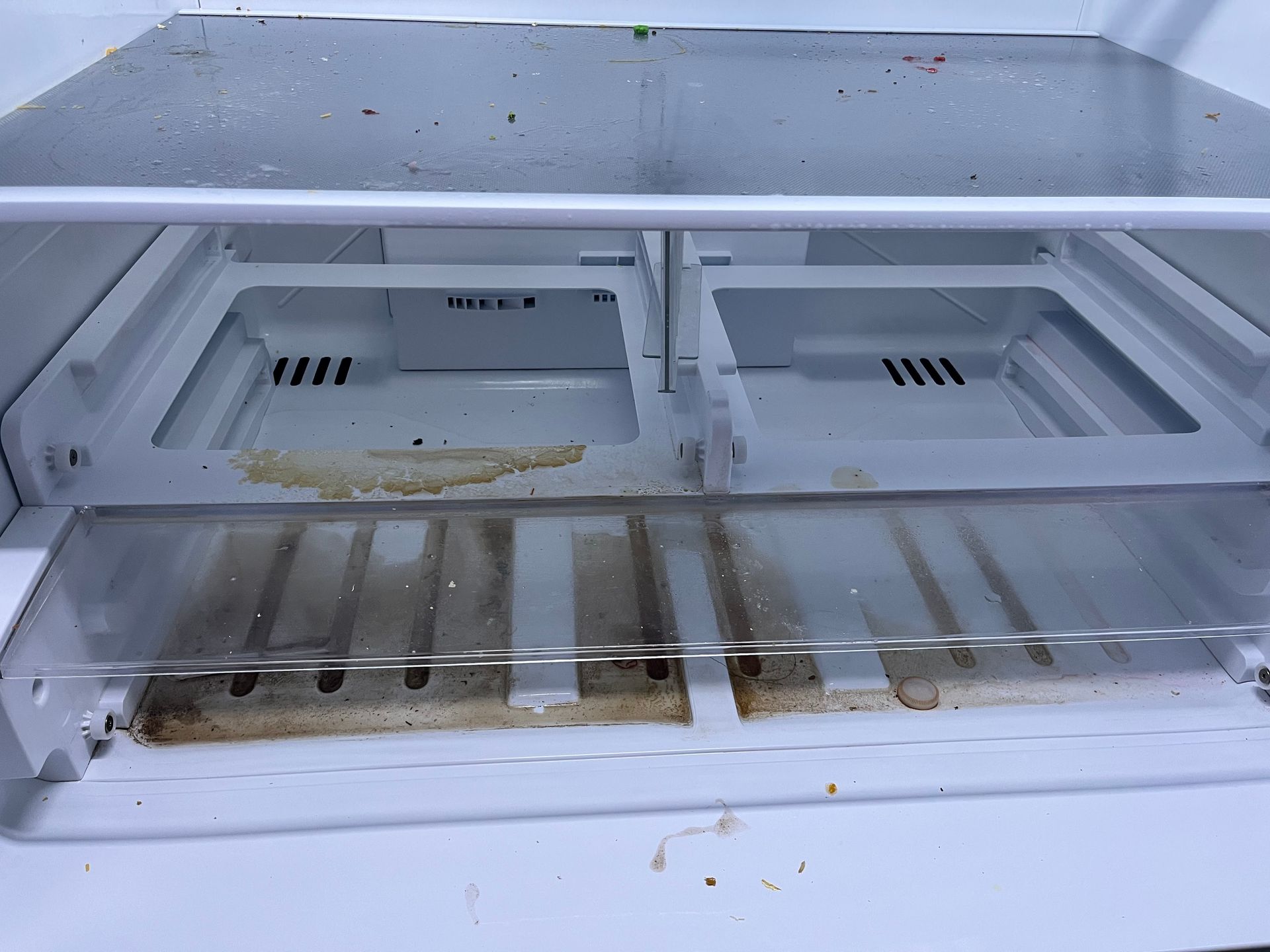 Inside of a white refrigerator with pull-out drawers, showing a dirty and dusty interior.
