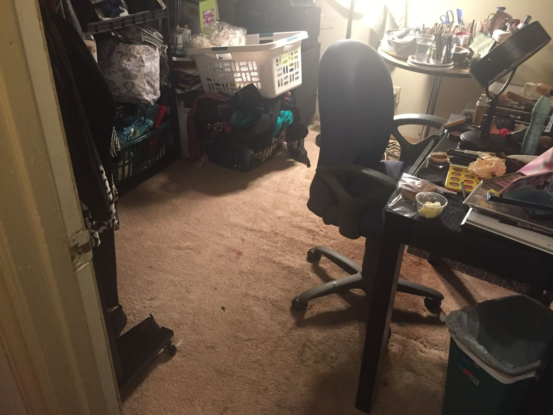Messy room with a desk, chair, and various items. The floor is carpeted, and there are cluttered shelves