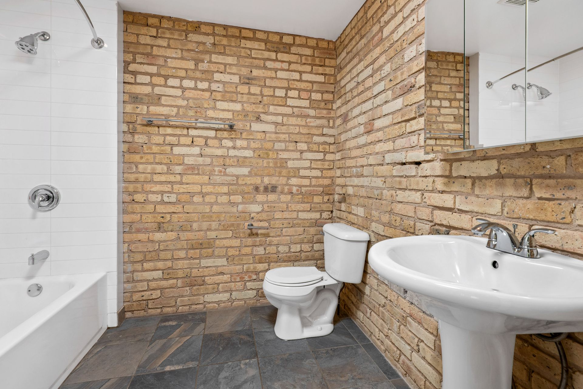 A bathroom with a toilet, sink, bathtub, and brick wall.