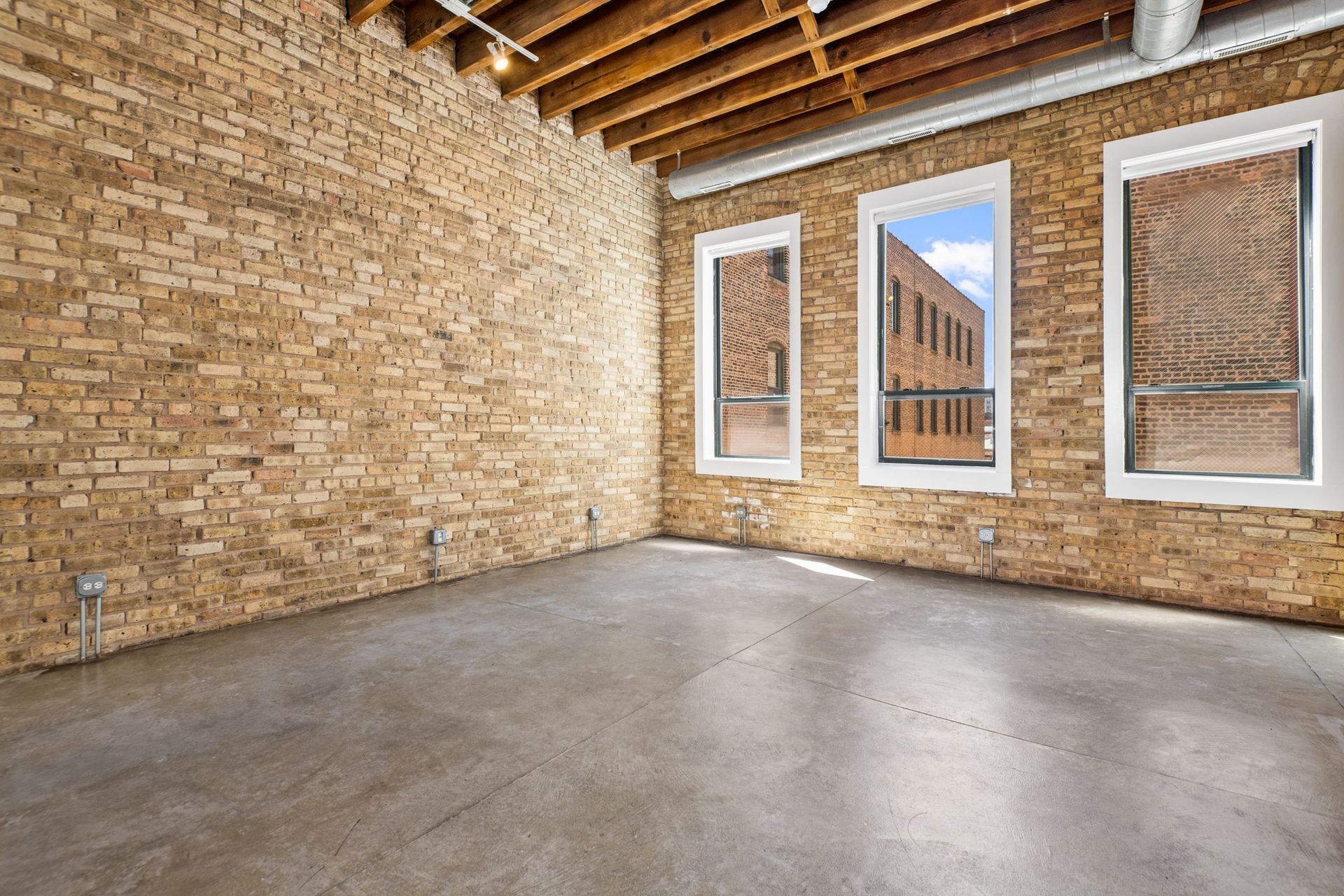 An empty room with a brick wall and three windows at 945 W Fulton Market Apartments.