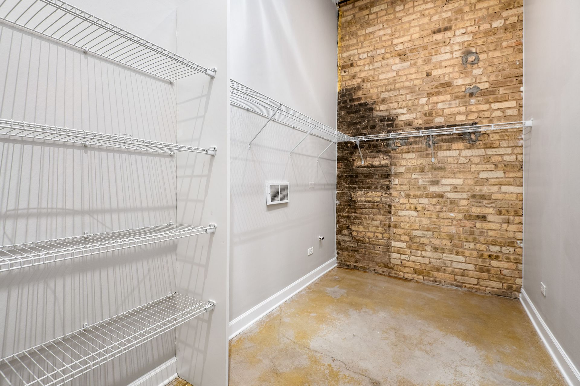 An empty closet with a brick wall and wire shelves.