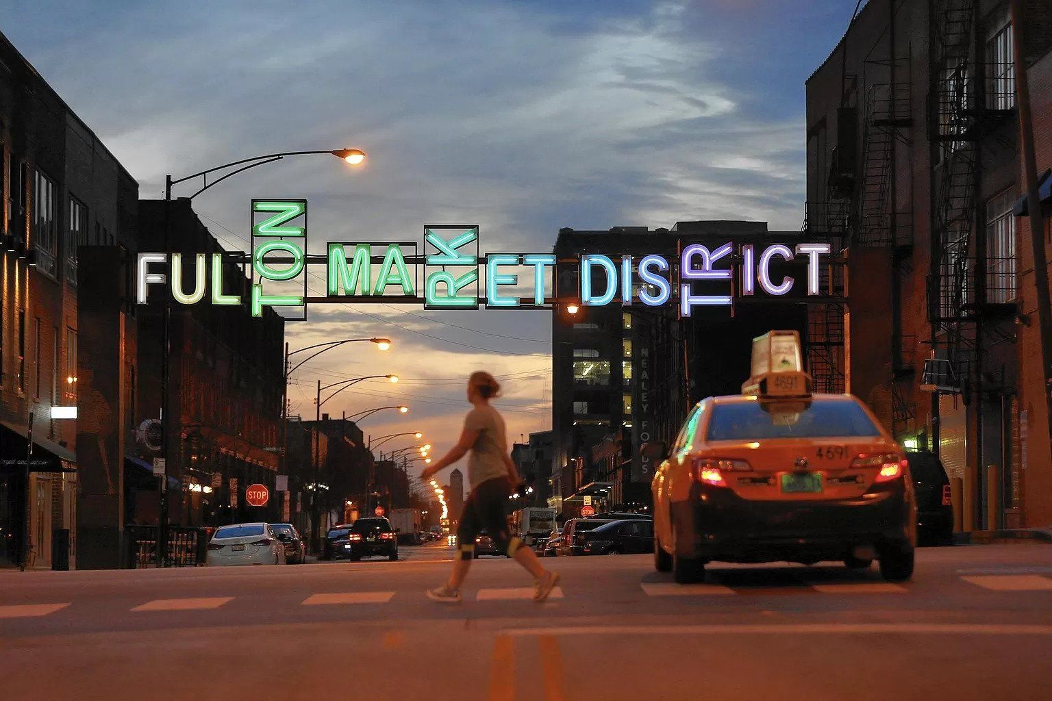 A man crosses a street in front of a sign that says full market district.